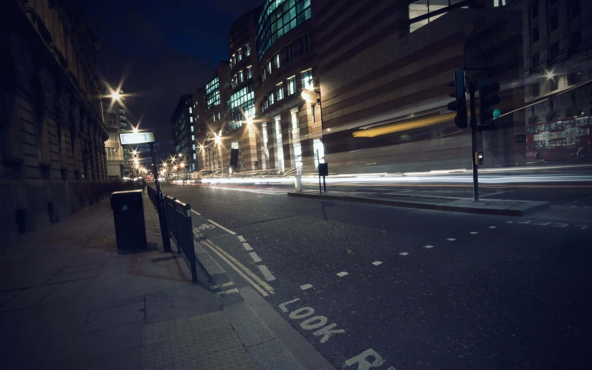 Night Street 桌布 壁紙 — 長時間曝光捕捉到在黑暗的城市街道上奔馳的汽車燈光軌跡，兩旁是發光的窗戶和街燈。