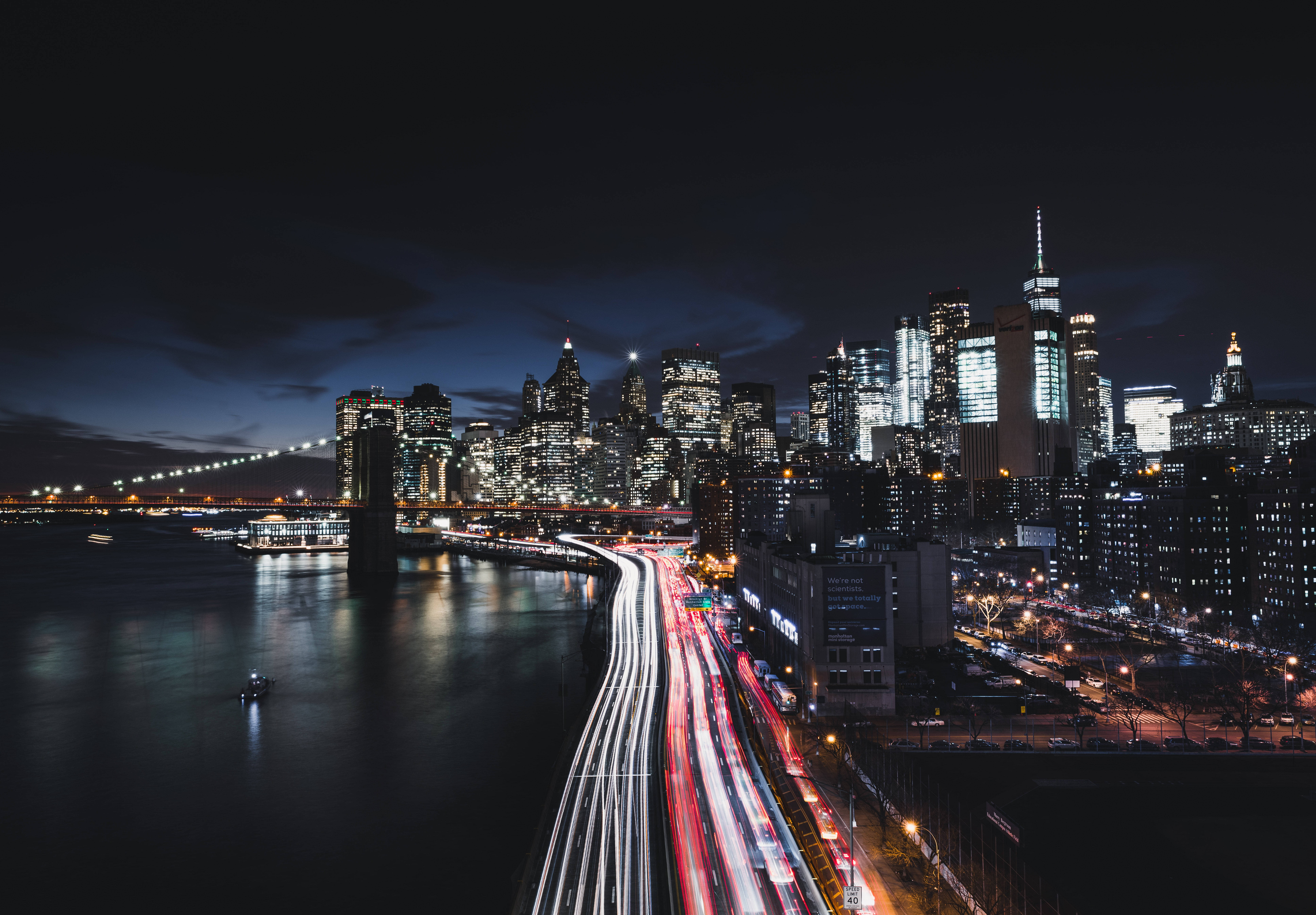 New York 桌布 壁紙 — 長時間曝光捕捉到夜間紐約市閃爍的天際線下，沿著海濱高速公路流動的車流所產生的紅色和白色光條。