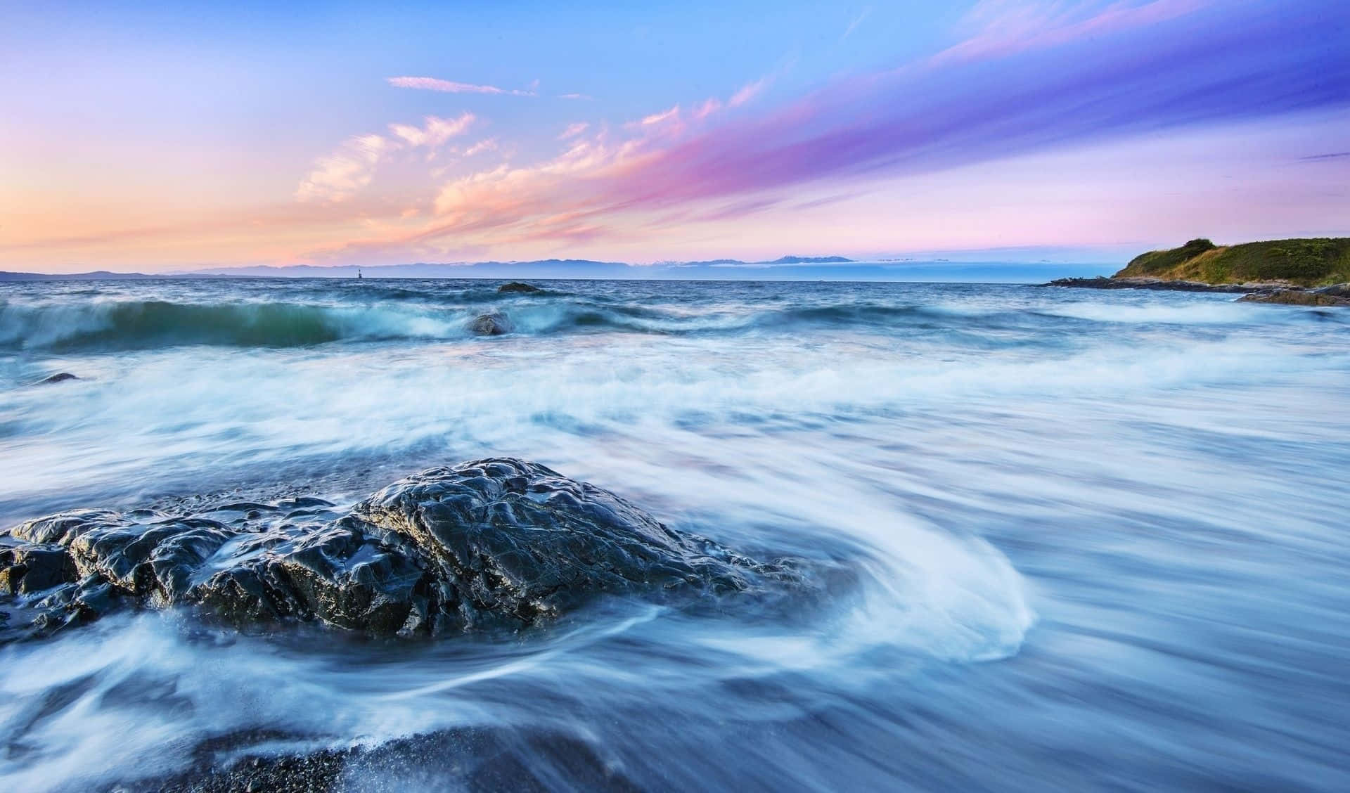 waves 桌布 壁紙 — 長時間曝光的海景捕捉到平滑的藍色水流在深色岩石周圍旋轉，天空呈現出充滿活力的紫色和粉紅色日落。