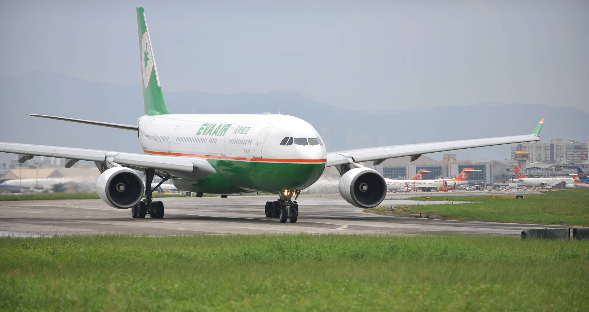 綠色和白色的長榮航空飛機在機場跑道滑行，背景有山脈。