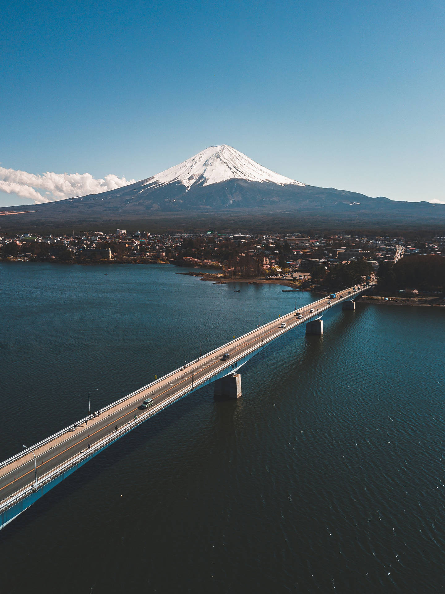 一座橋橫跨湖泊，遠處的富士山在清澈的藍天下。
