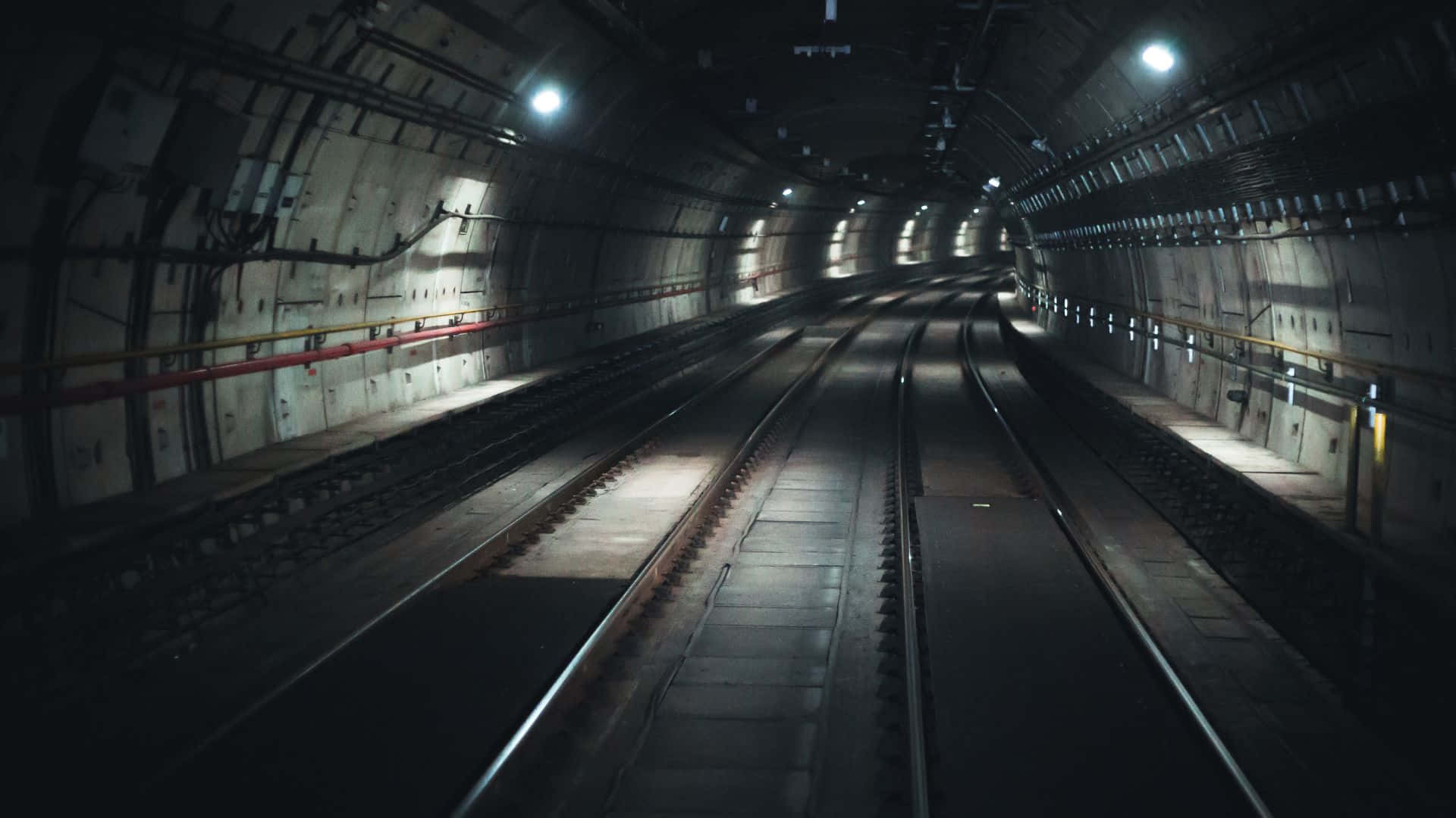 Subway 桌布 壁紙 — 長而黑暗的地鐵隧道，平行嘅火車軌道被稀疏嘅天花燈照亮，一直延伸到遠方。