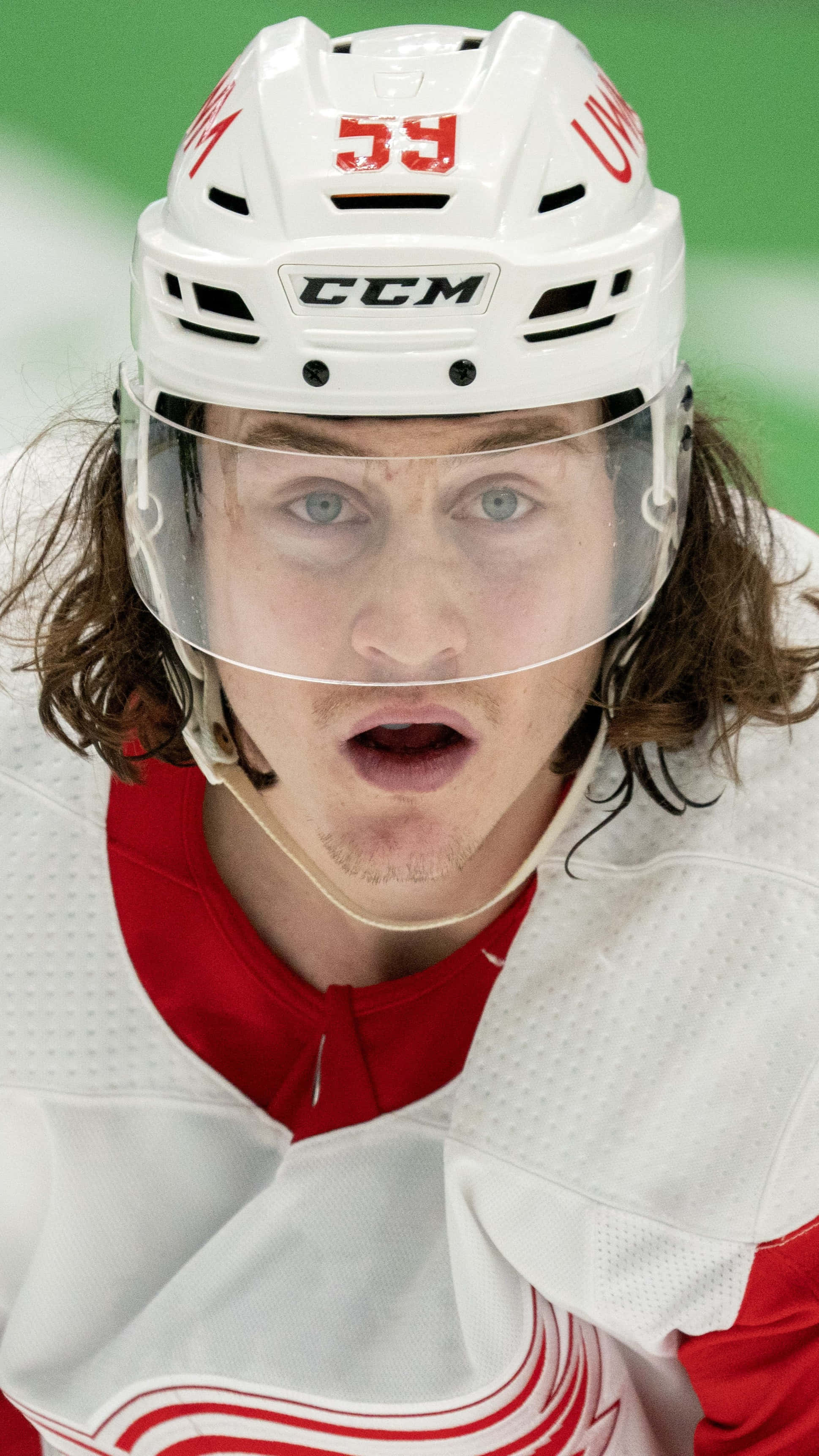 Tyler Bertuzzi 桌布 壁紙 — 長髮冰球運動員的近距離特寫，戴著白色頭盔和紅色球衣，專注地向前看。
