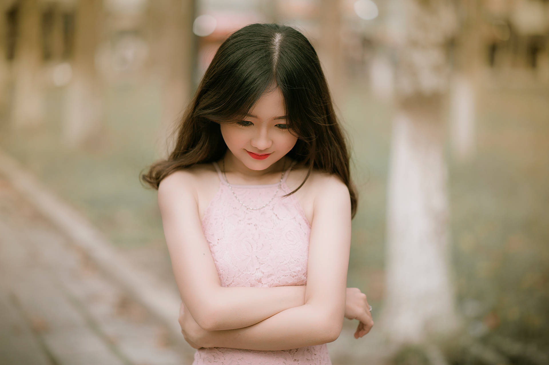 年輕女性身穿粉紅色蕾絲連衣裙，在戶外交叉雙臂站立。
