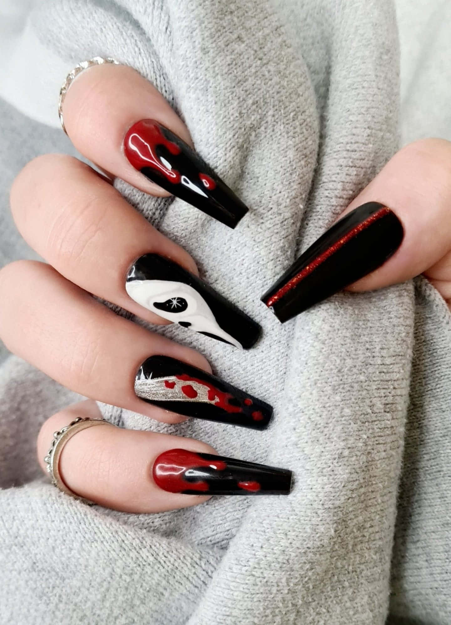 Halloween Nail Art 桌布 壁紙 — 長黑色細高跟指甲搭配紅色閃粉和血跡飛濺設計，放在柔軟的灰色毛衣袖子上。