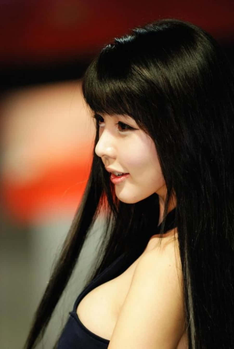 長黑髮的年輕女性在室內紅色背景前溫柔微笑。