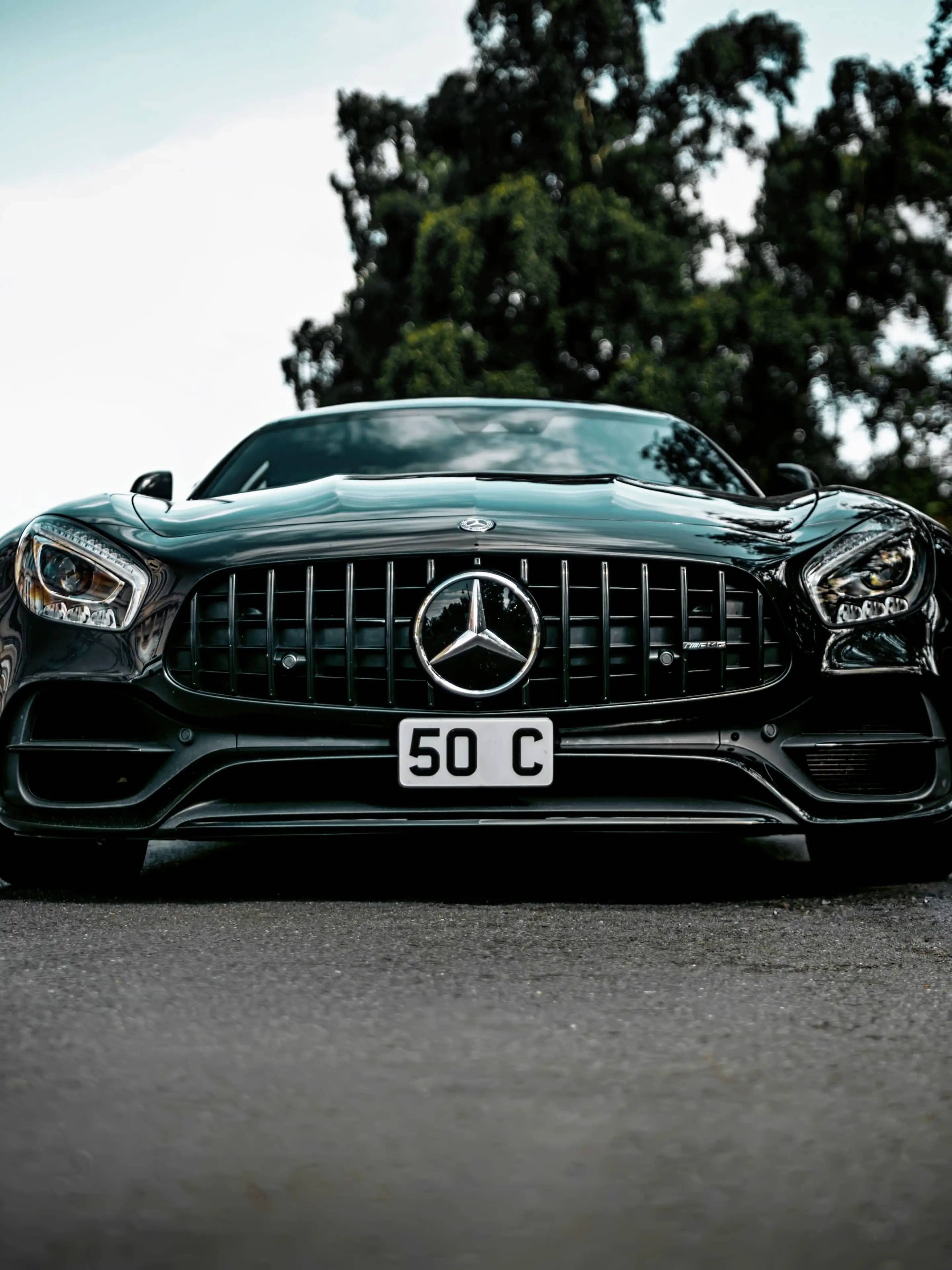 閃亮AMG車頭正面 壁紙 — 一架時尚的黑色 Mercedes-AMG GT 停泊在瀝青路上，背景有樹木，天空晴朗。