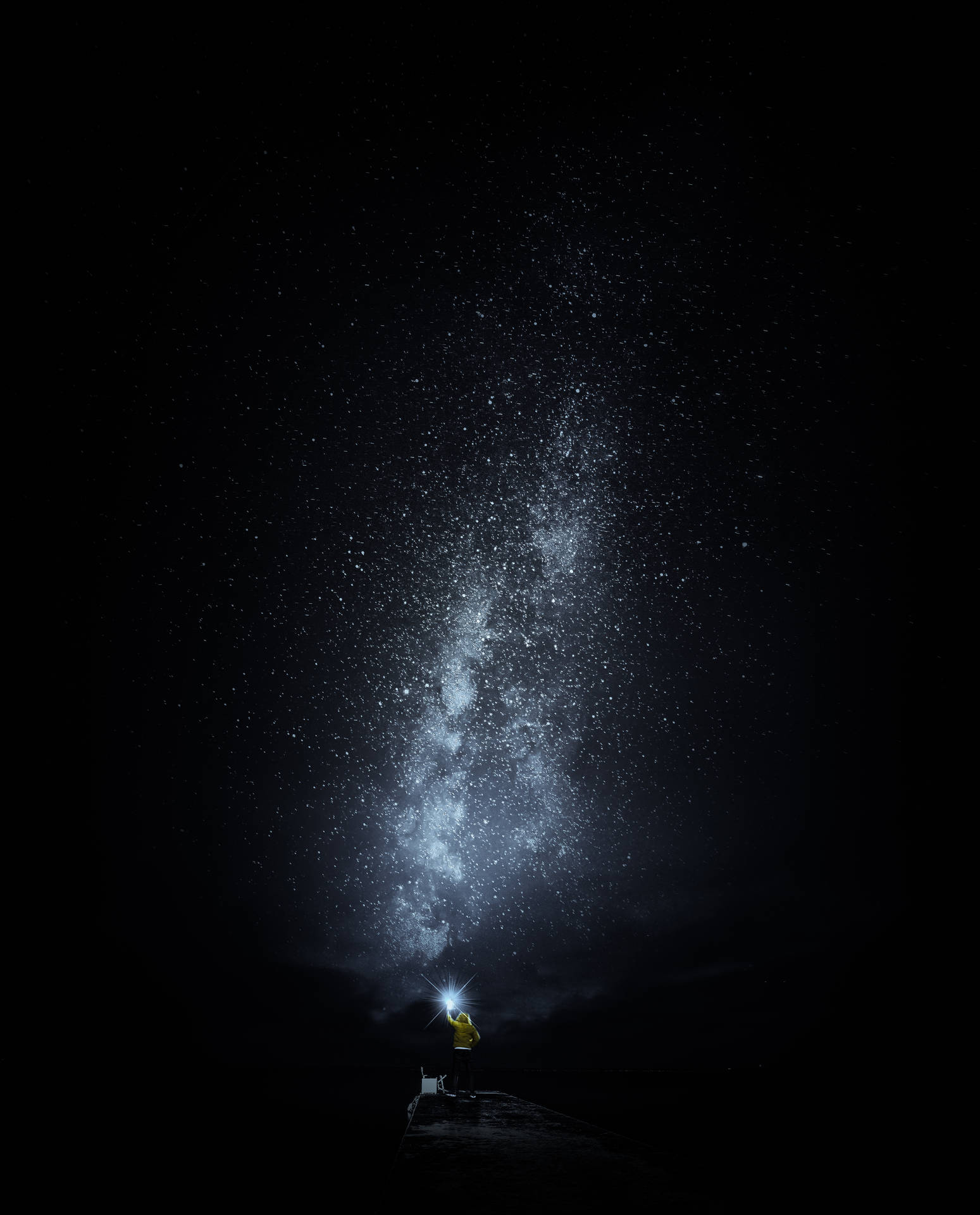 穿黃色外套的人晚上用手電筒照射銀河星星。