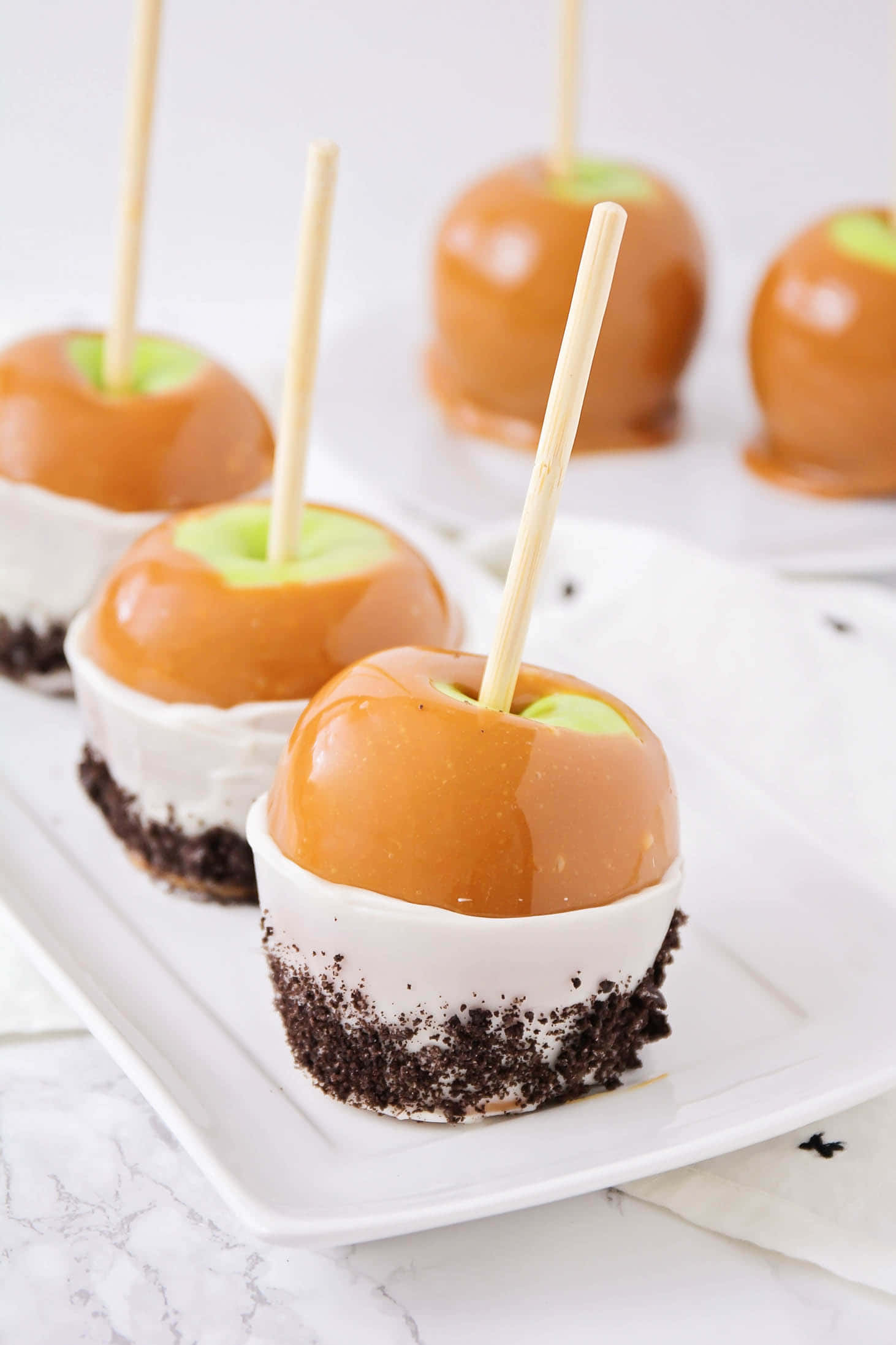 Caramel Apples 桌布 壁紙 — 閃亮焦糖蘋果置於白色忌廉和朱古力碎餅底上，放在白色碟中。