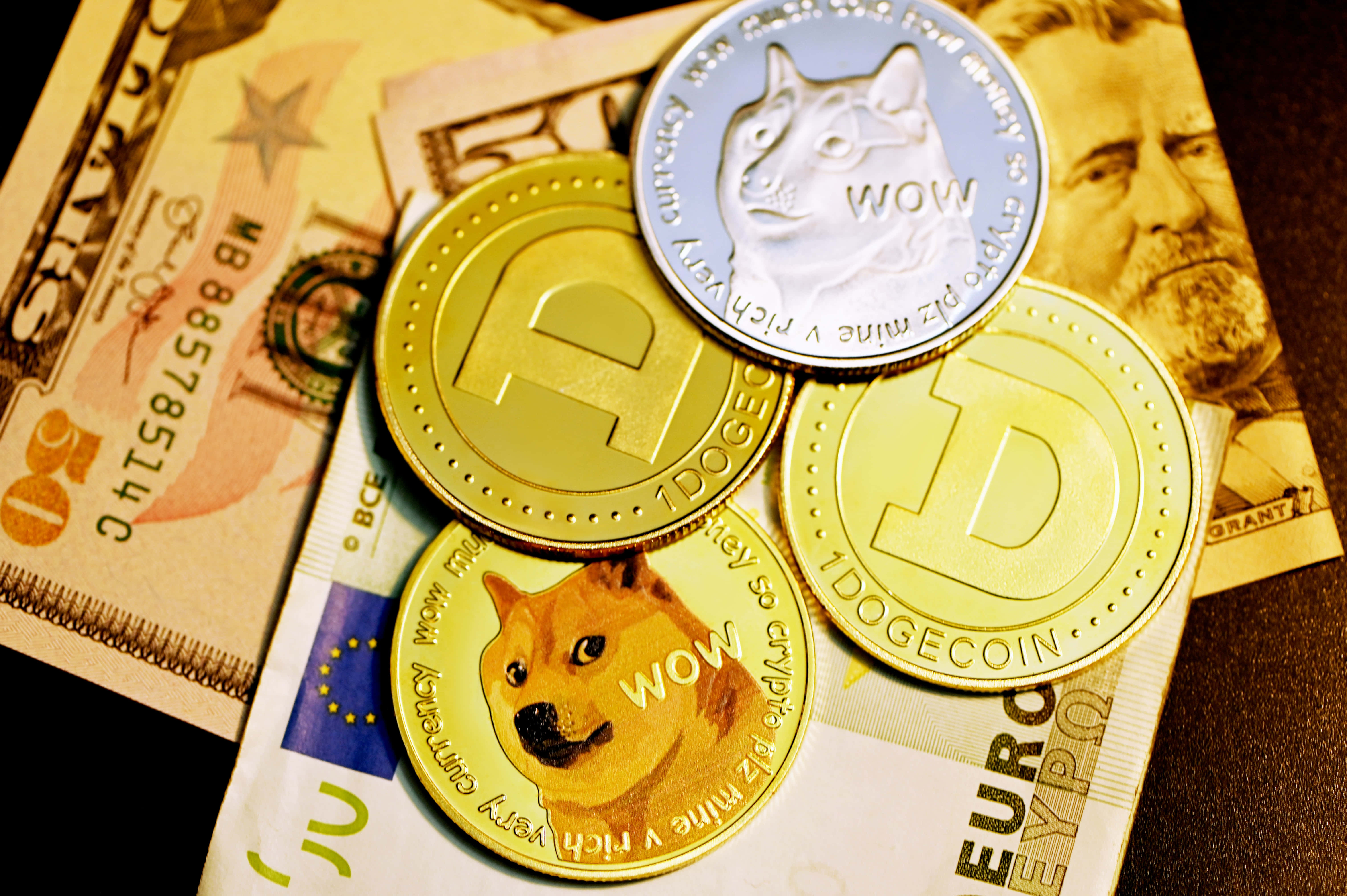 Dogecoin 桌布 壁紙 — 閃亮的狗狗幣代幣放在一堆美元和歐元紙幣上，在溫暖的燈光下。