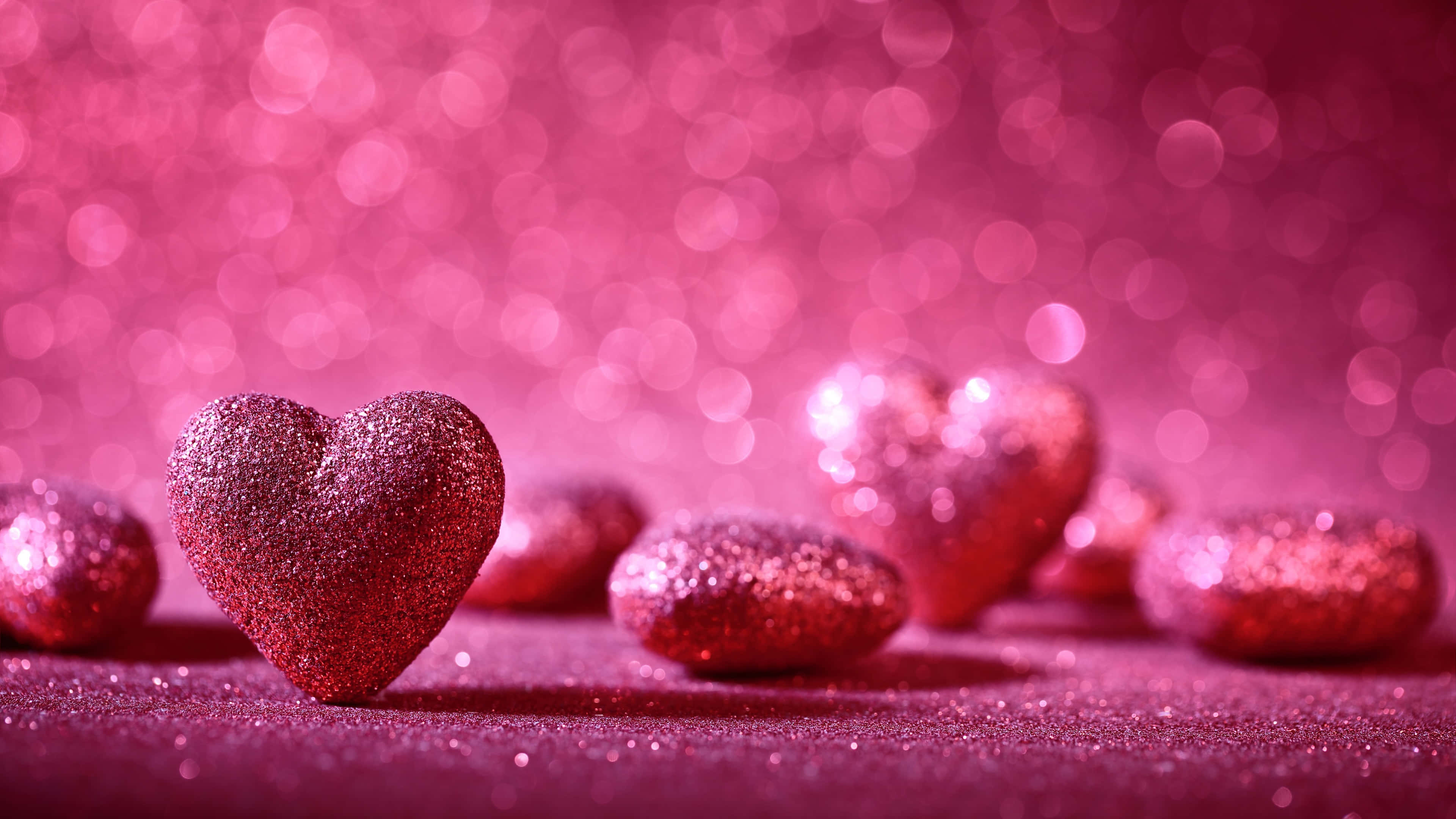 Pink Love 桌布 壁紙 — 閃亮的粉紅色閃粉心形散落在閃爍的表面上，帶有夢幻般的散景背景。