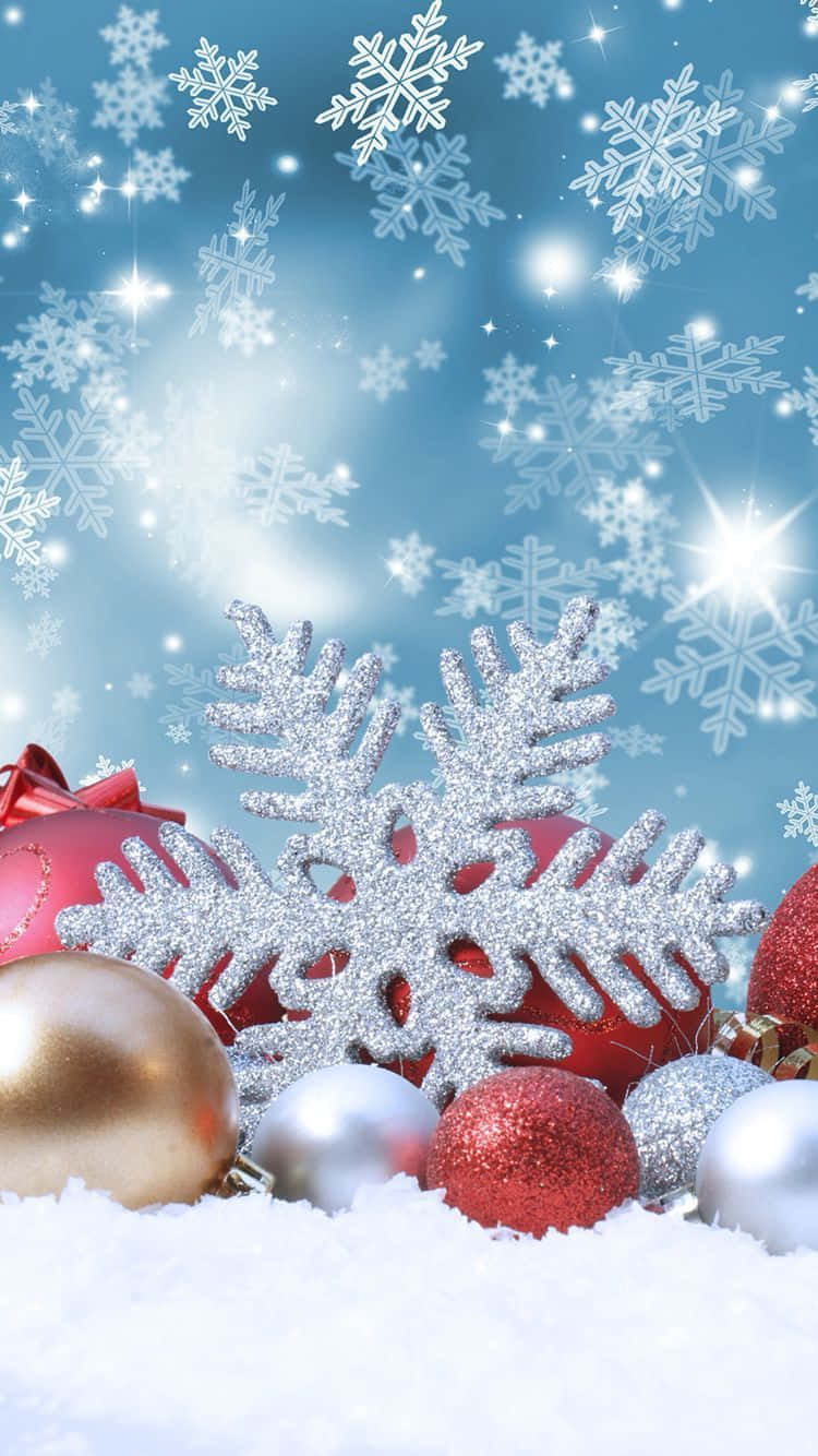 Winter Holiday 桌布 壁紙 — 閃亮的紅色、金色和銀色聖誕裝飾品依偎在雪中，閃爍的雪花在明亮的藍天下飄落。