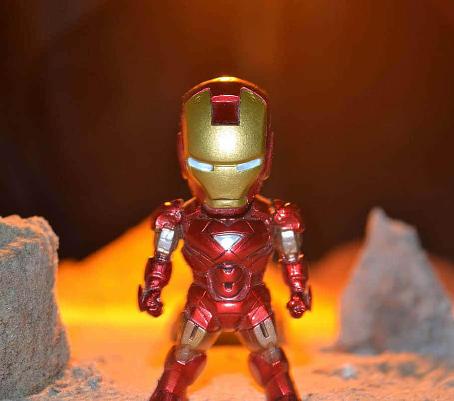 Iron Man Bobbleheads 桌布 壁紙 — 閃亮的紅色和金色鐵甲奇俠動作人偶在溫暖光芒下英勇地站在岩石地形上。