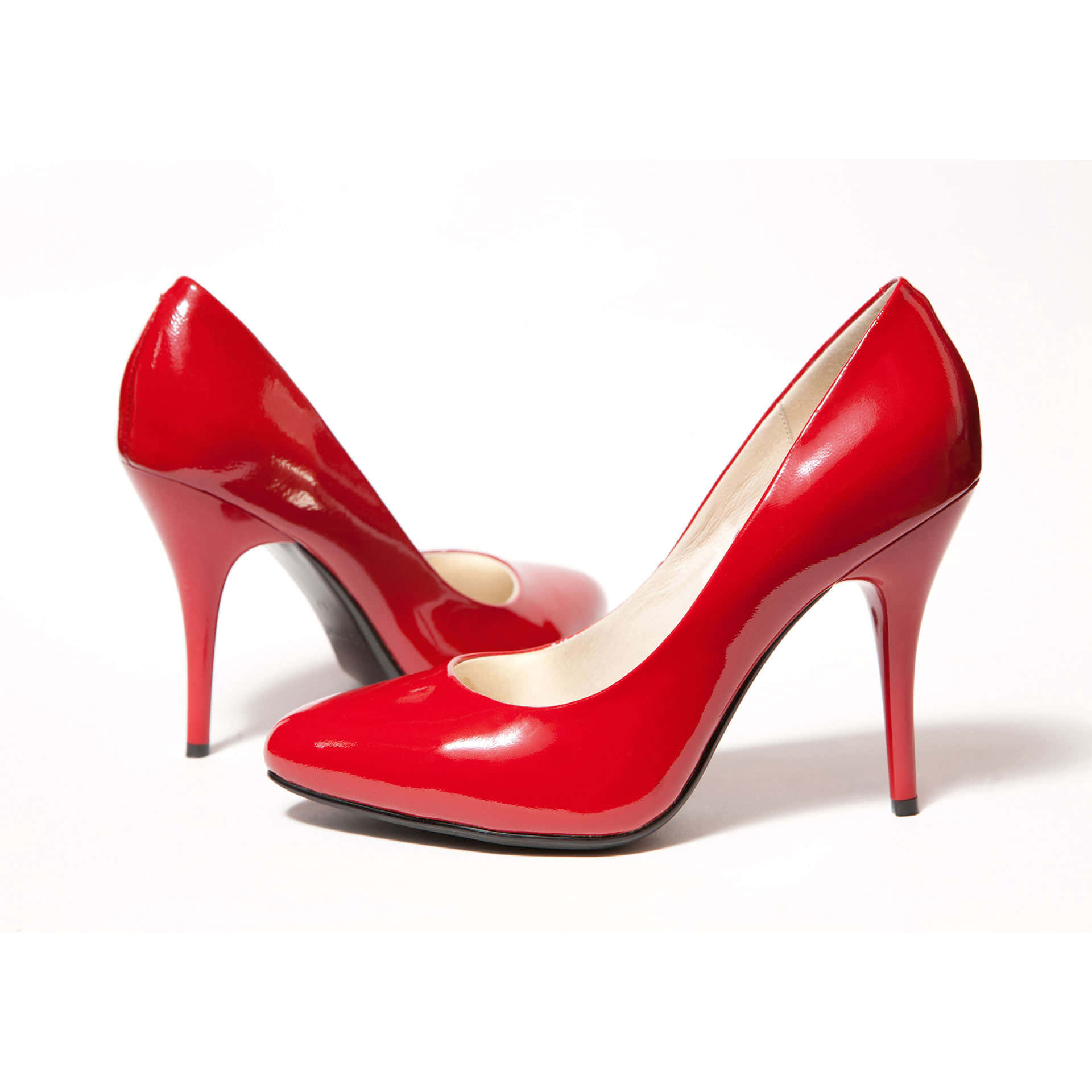 Red High Heels 桌布 壁紙 — 閃亮的紅色漆皮高跟鞋，配以纖細的細跟和奶油色鞋墊，置於潔淨的白色背景上。