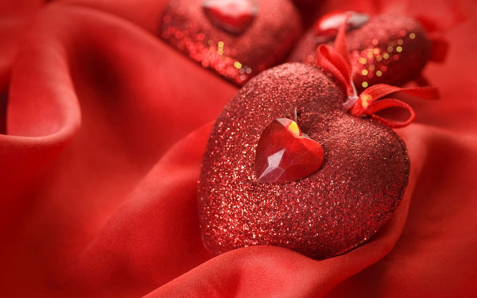 3d Heart 桌布 壁紙 — 閃亮的紅色閃粉心形飾以水晶點綴，在特寫鏡頭中放置於豪華的紅色緞面布料上。