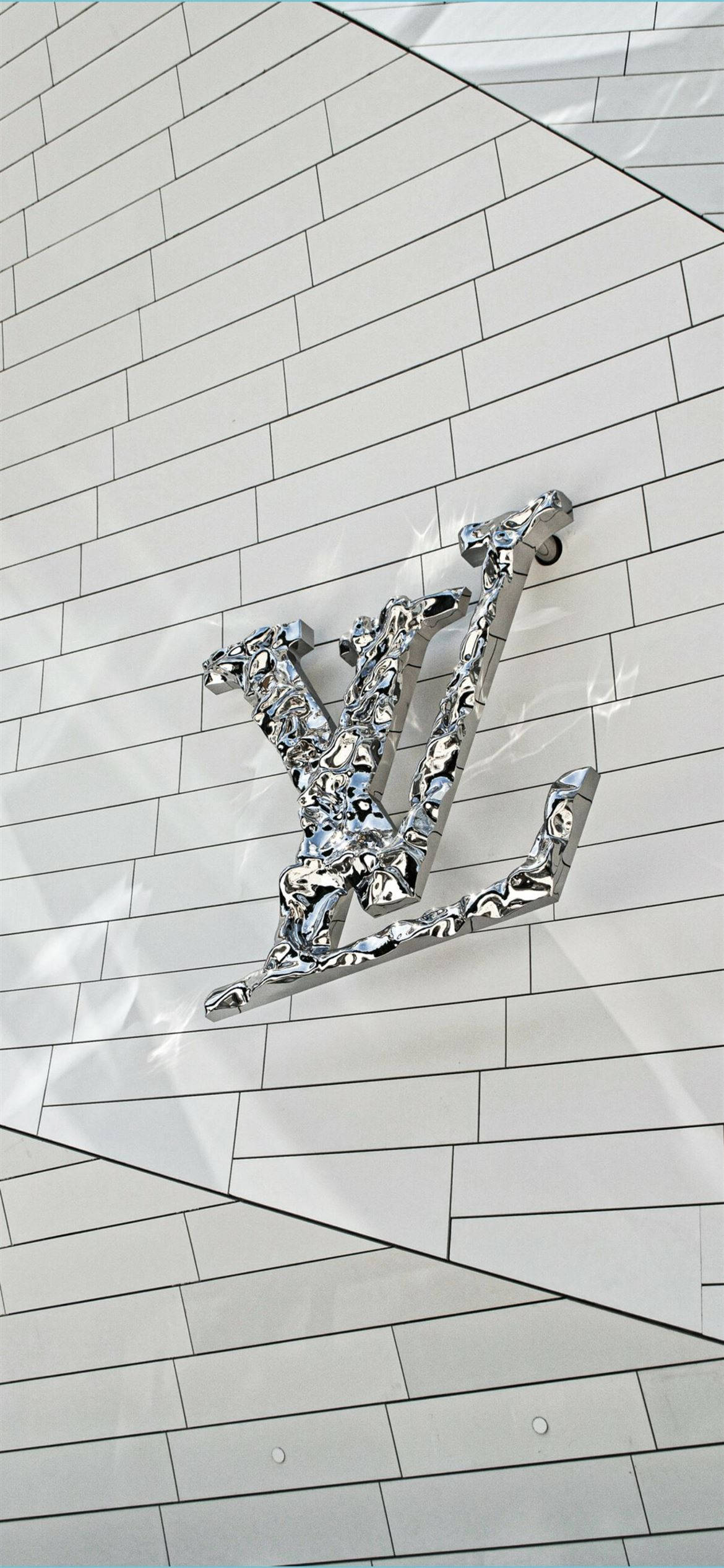 金屬動態圖 桌布 壁紙 — 閃亮的鉻色 Louis Vuitton 標誌安裝在帶有幾何對角線的白色瓷磚牆上。