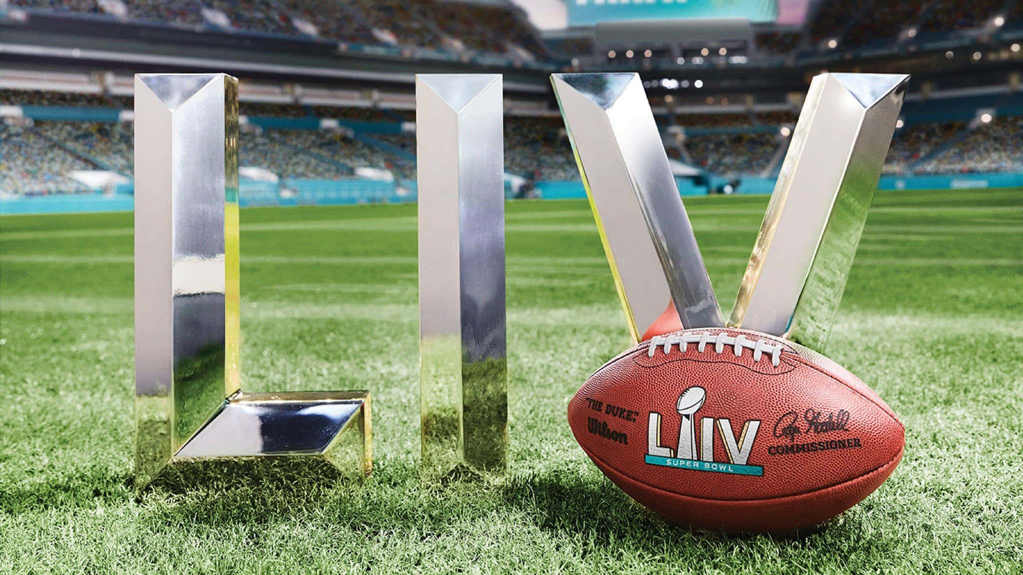 Super Bowl 桌布 壁紙 — 閃亮的銀色超級碗LIIV獎盃字母和官方足球在明亮的日光下放置在充滿活力的綠色體育場草坪上。