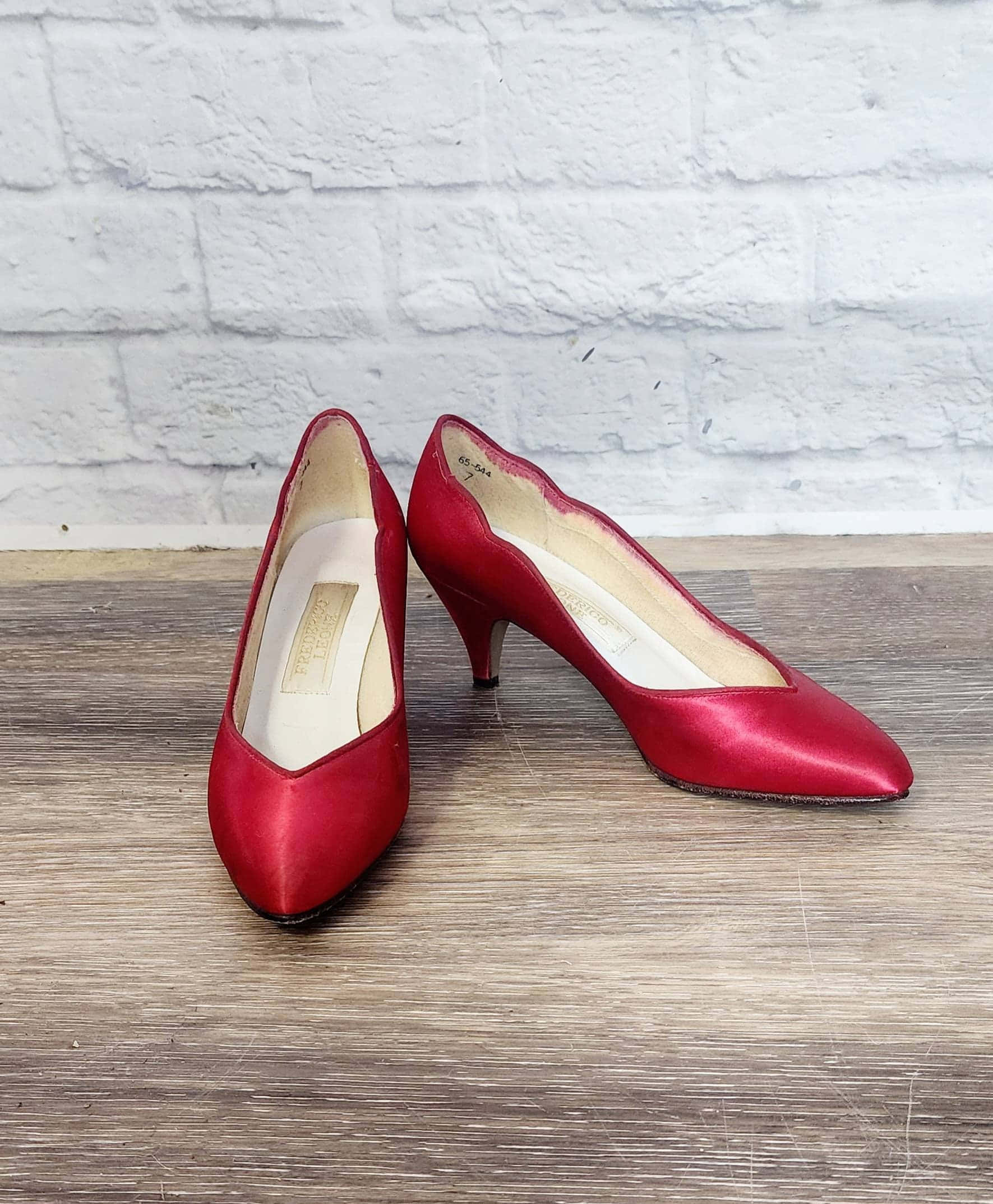 Red Shoes 桌布 壁紙 — 閃亮紅色緞面尖頭高跟鞋放在木地板上，背景是白色磚牆。