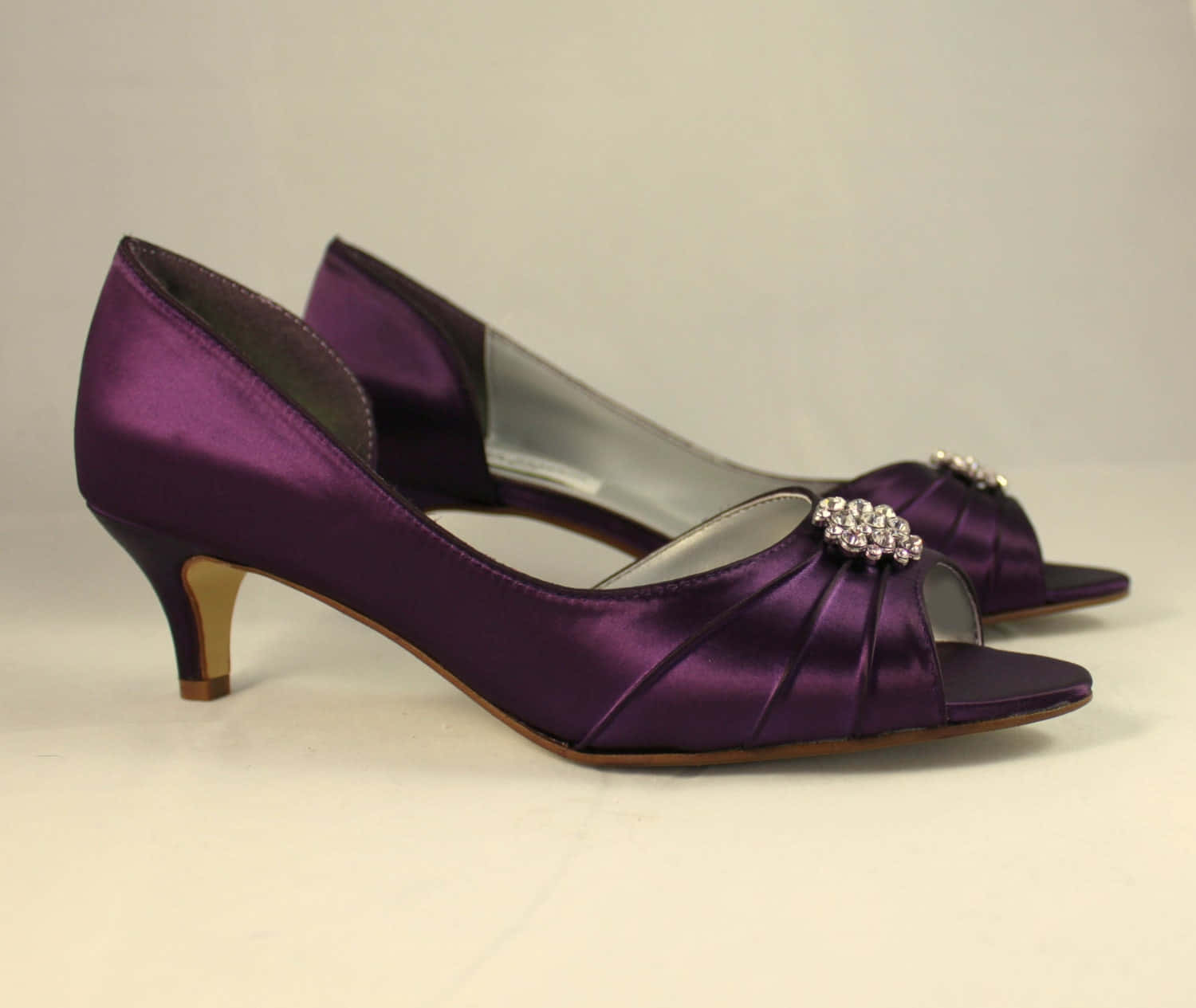 Purple Shoes 桌布 壁紙 — 閃亮紫色緞面魚嘴高跟鞋，飾有水晶裝飾和金色鞋跟，置於純白表面上。