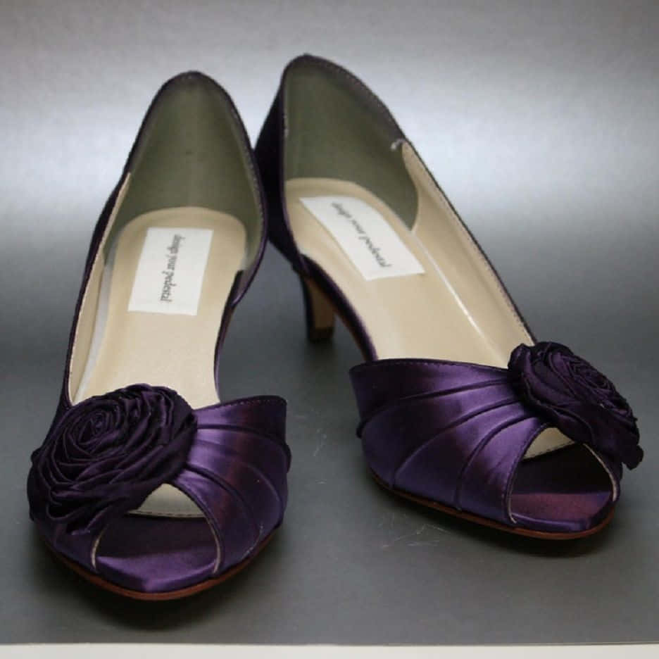 Purple Shoes 桌布 壁紙 — 閃亮紫色緞面魚嘴高跟鞋，飾有花卉蝴蝶結，優雅地放置在灰色中性表面上。
