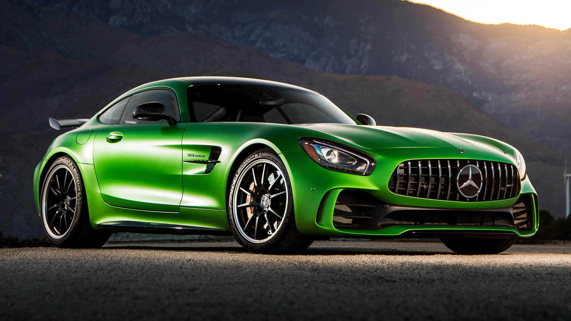 閃亮綠色梅賽德斯-AMG GT R 背景 壁紙 — 一輛充滿活力的綠色Mercedes-AMG GT跑車在崎嶇的山地地形上，於金色夕陽下閃耀光芒。