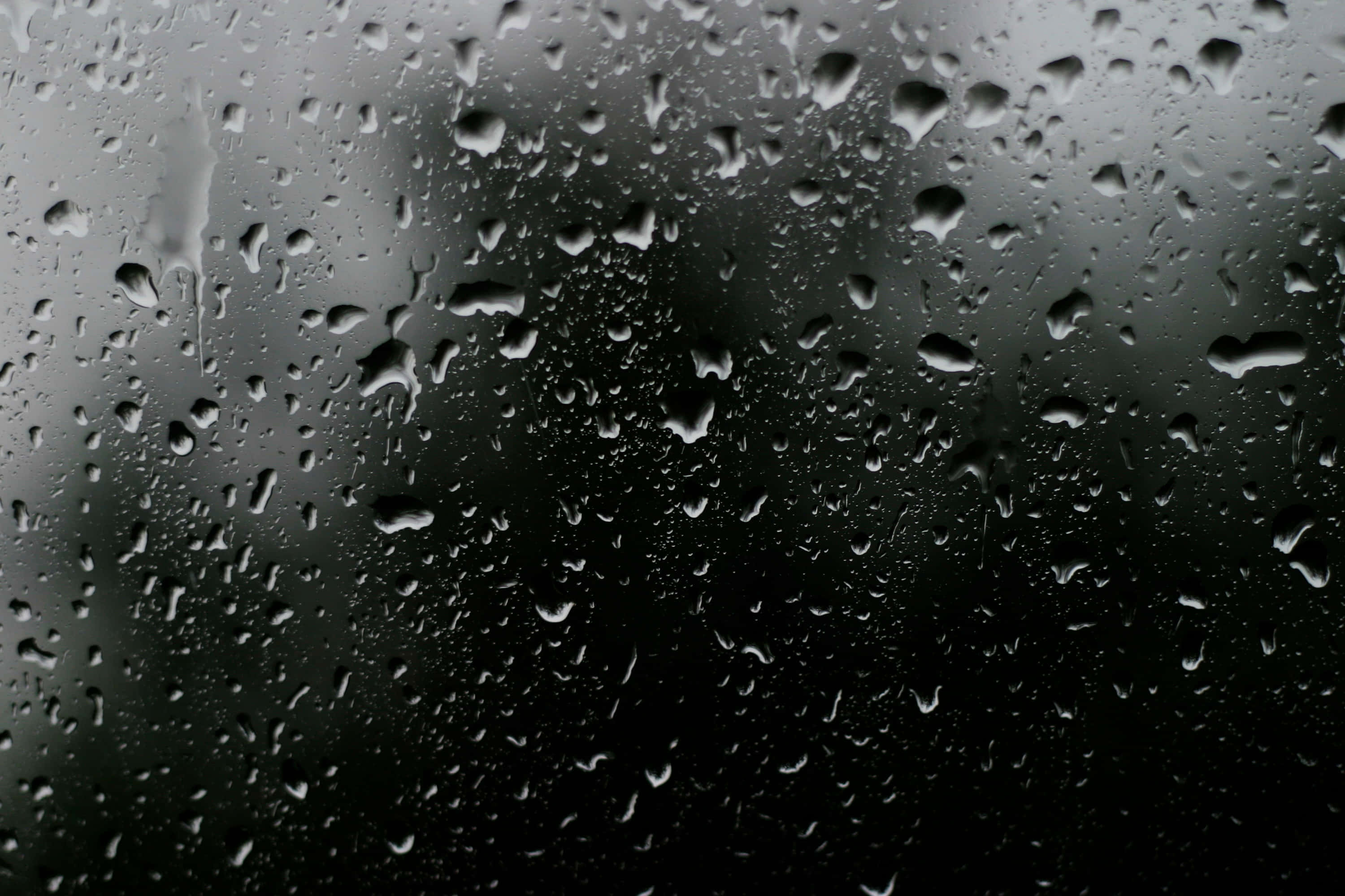 閃亮藍色水紋特寫 壁紙 — 雨滴依附在玻璃表面，將黑暗的戶外場景模糊成柔和的灰色調。