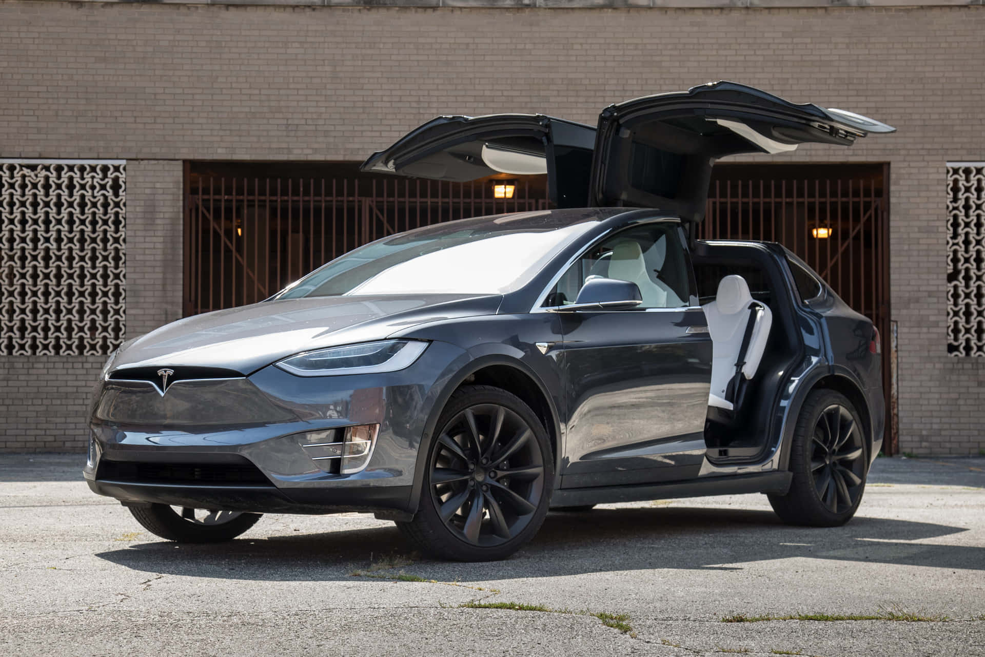 深灰色 Tesla Model X 展開鷹翼門，停在磚砌建築前。