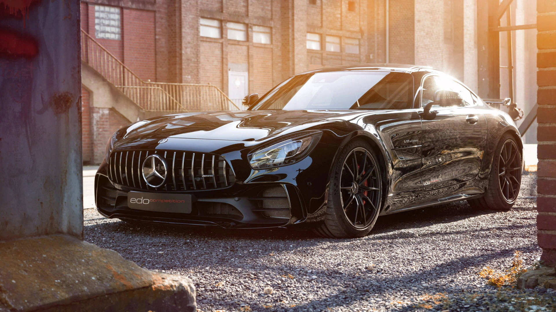 黑色Mercedes-AMG GT停在磚砌建築之間的礫石上，金色時光。