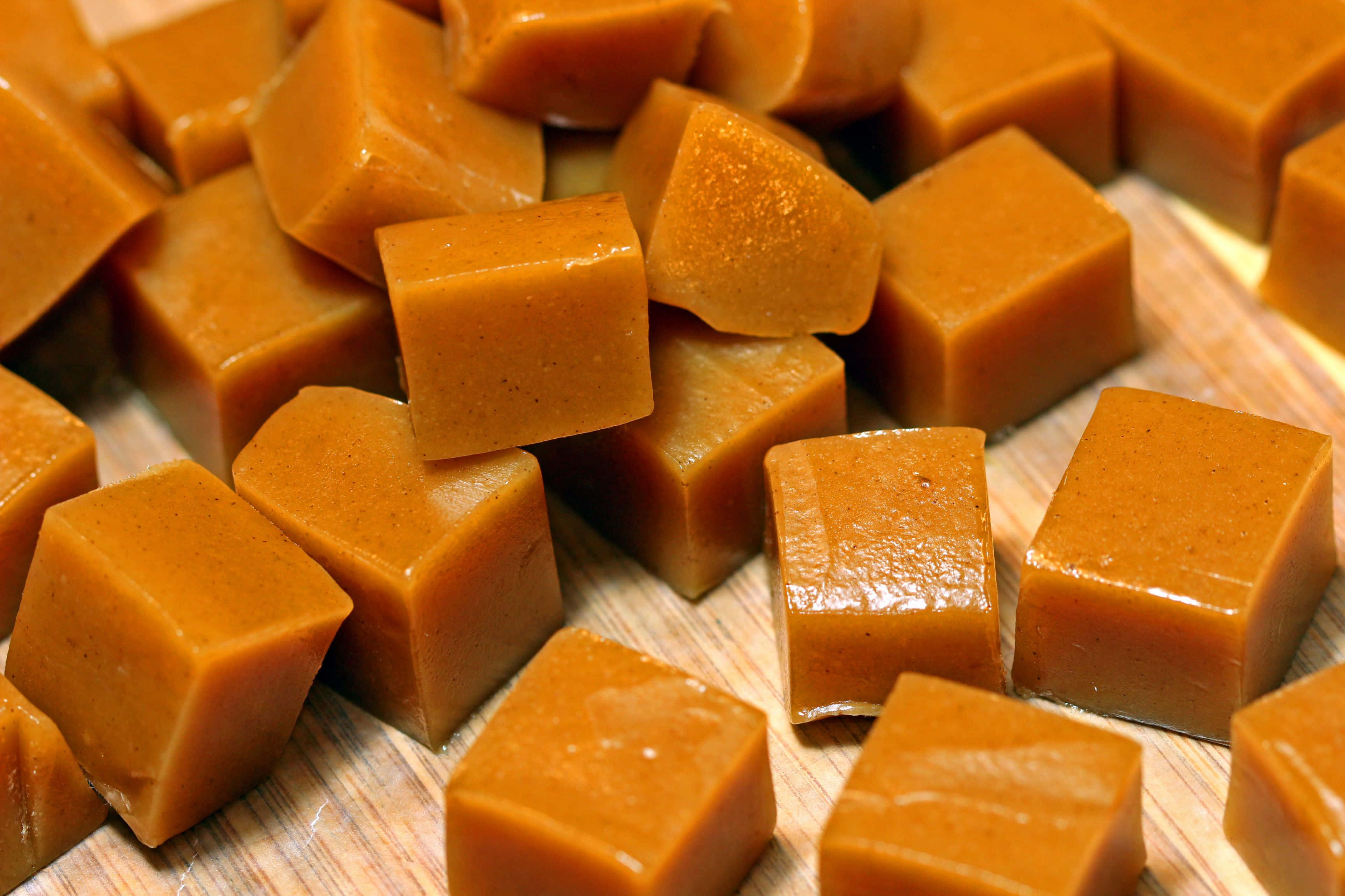 Brown Caramel 桌布 壁紙 — 閃爍琥珀色焦糖糖果完美立方體散落在溫暖的木質表面上。