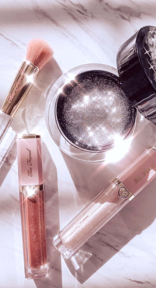 Cute Makeup 桌布 壁紙 — 閃爍的化妝產品，包括閃粉和唇彩，排列在帶有柔和光線的大理石表面上。