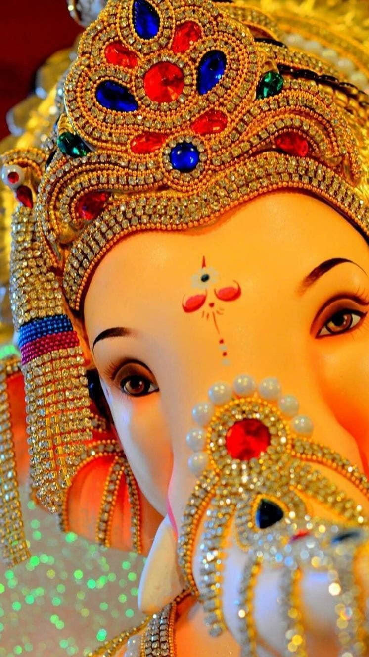 ganesh iPhone 桌布 壁紙 — 閃爍金色象神雕像的特寫，飾有紅、藍、綠色寶石，背景閃閃發光。