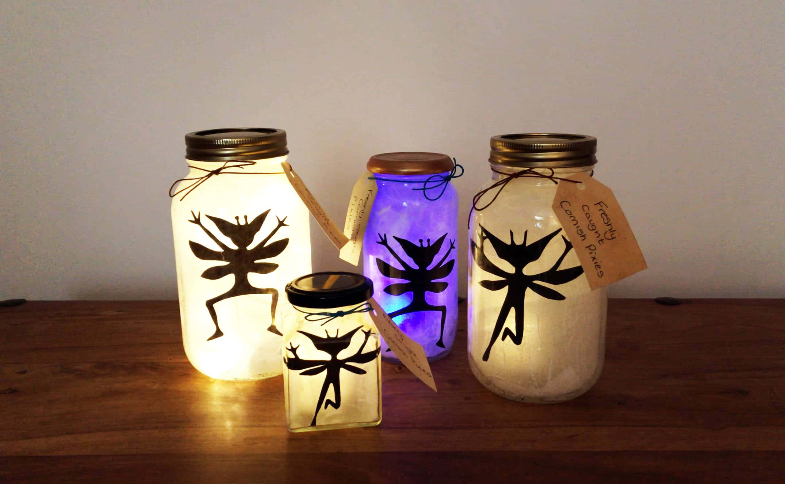 閃耀如星 壁紙 — 四個發光的玻璃瓶帶有仙女剪影，在素牆前將溫暖的光線投射在木質表面上。