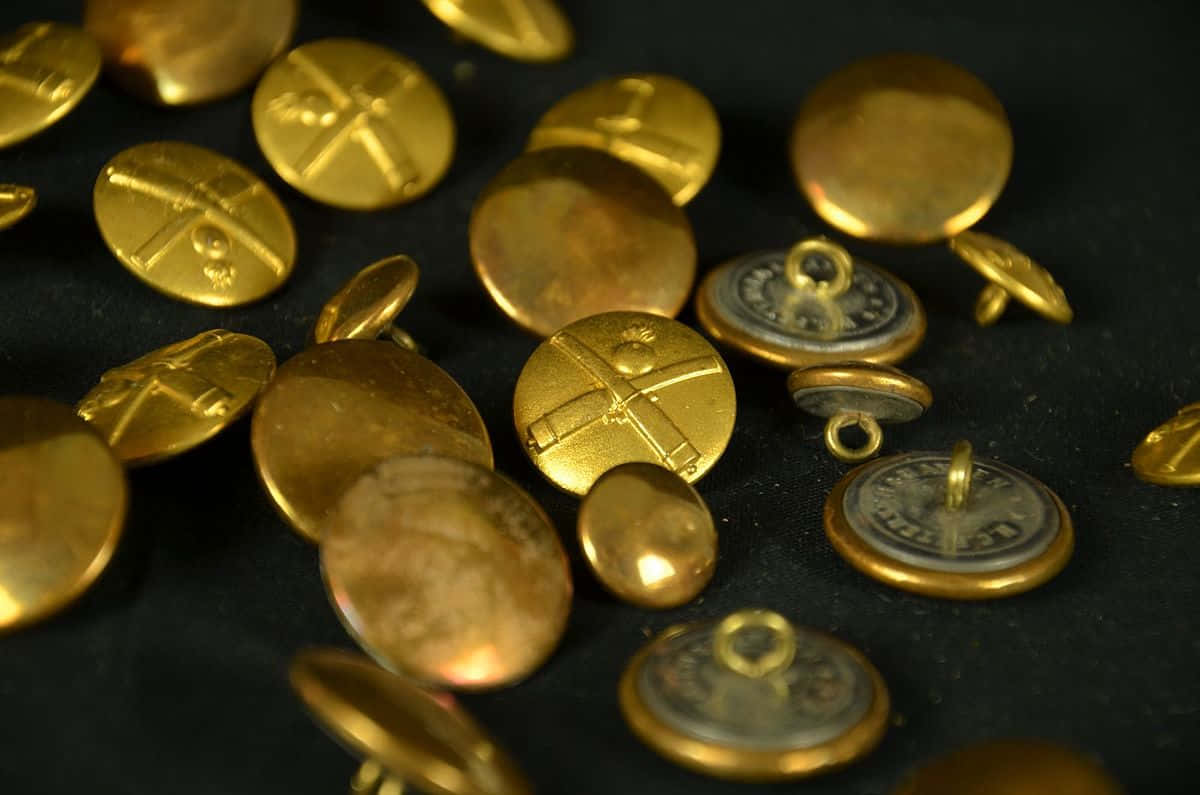 閃耀的彩色按鈕排 壁紙 — 金色復古鈕扣帶有雕刻十字圖案，散落在深色紋理表面上。