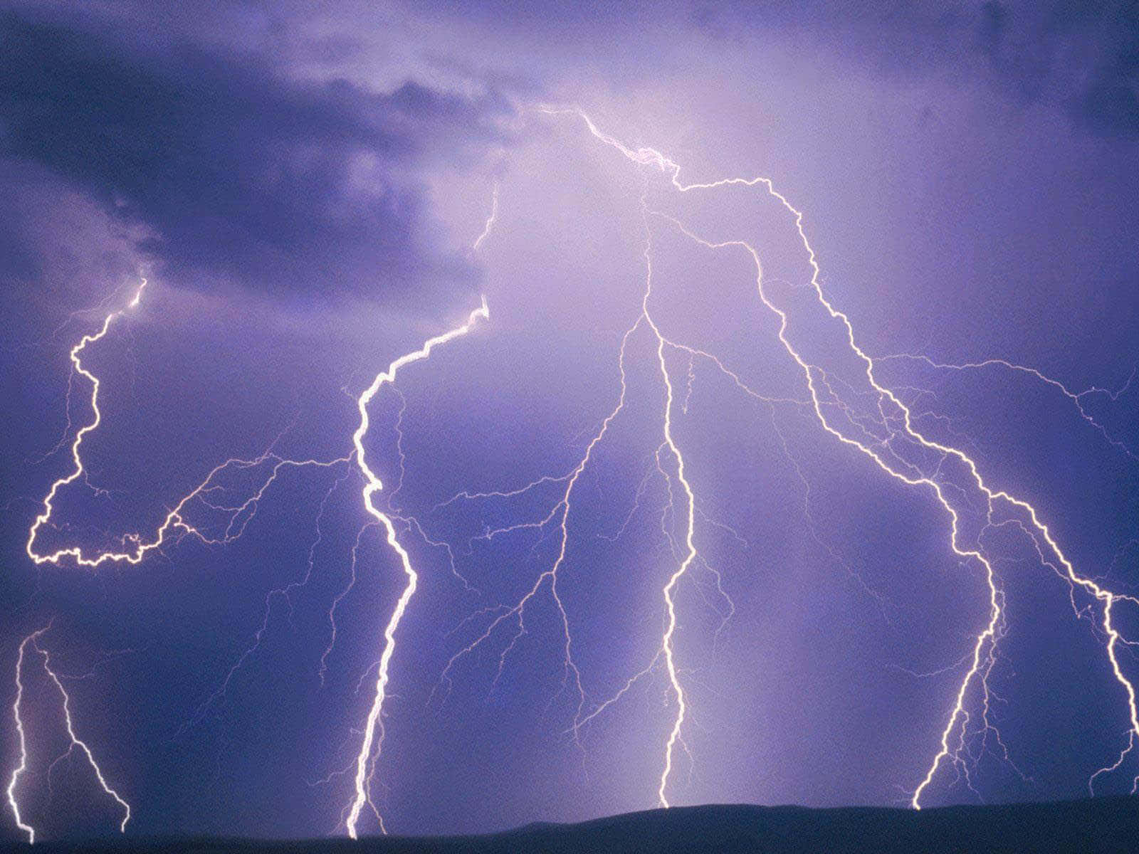強烈的閃電劃過黑暗地平線上方暴風雨般的紫色天空。