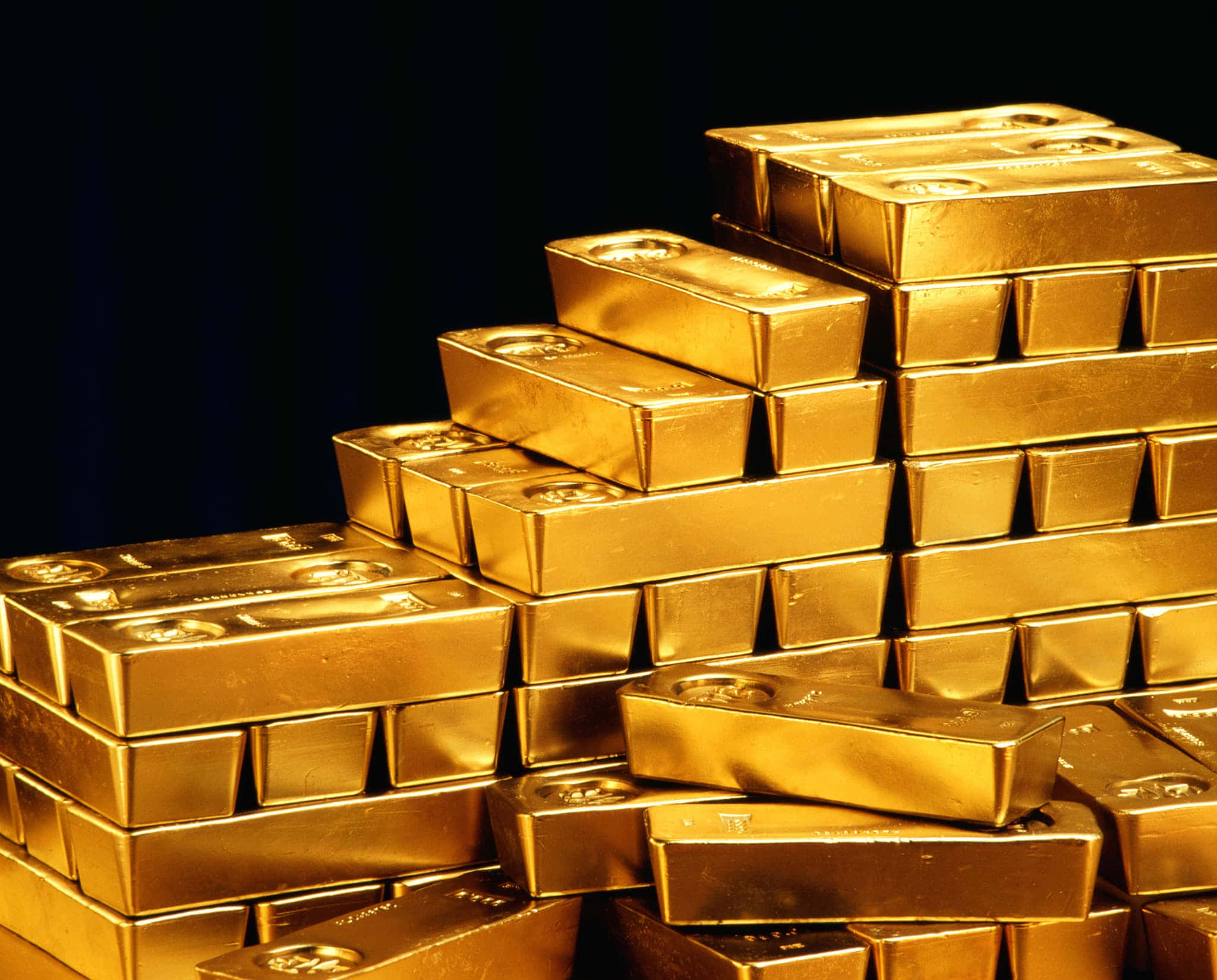 閃耀的金條 壁紙 — 一堆閃閃發光的金條以金字塔形排列在深色背景上。