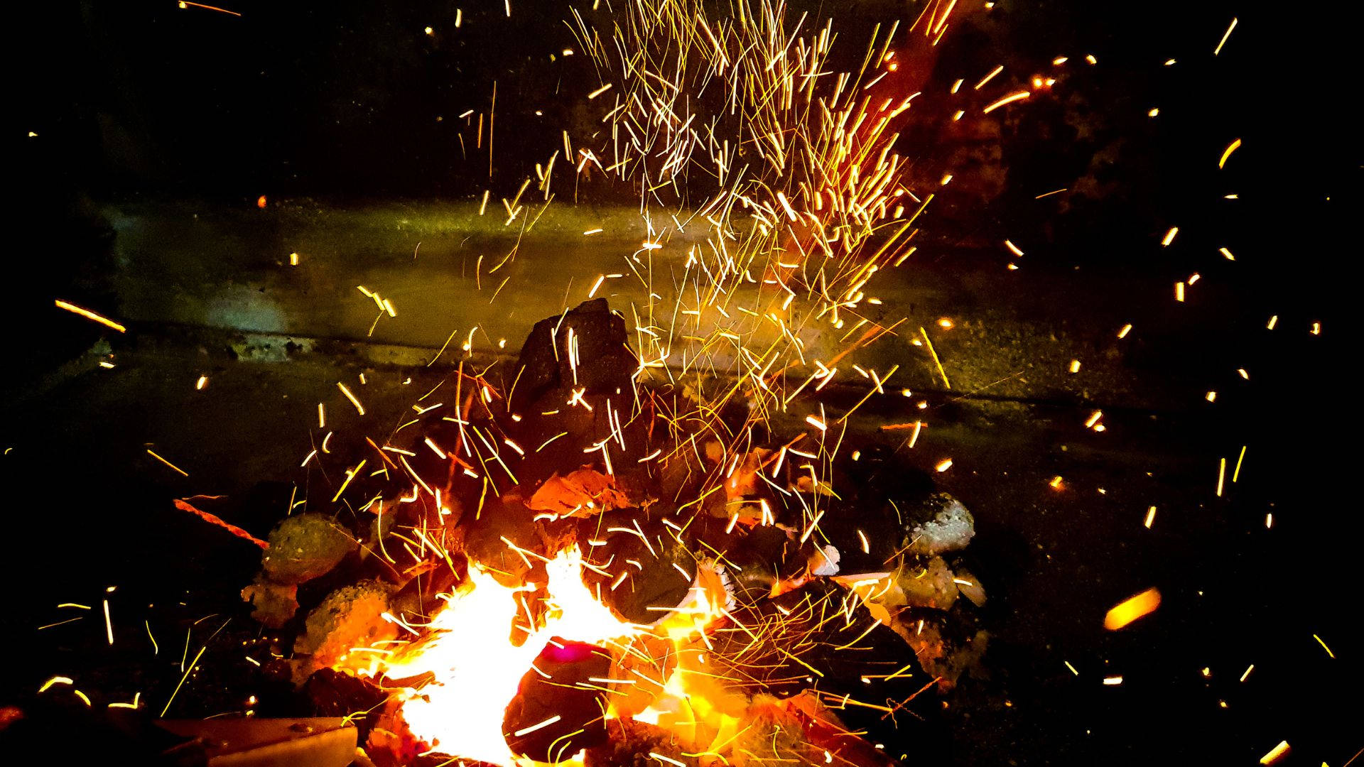 閃耀篝火熱力 壁紙 — 夜晚咆哮的營火在黑暗背景下飛舞著金色火花。