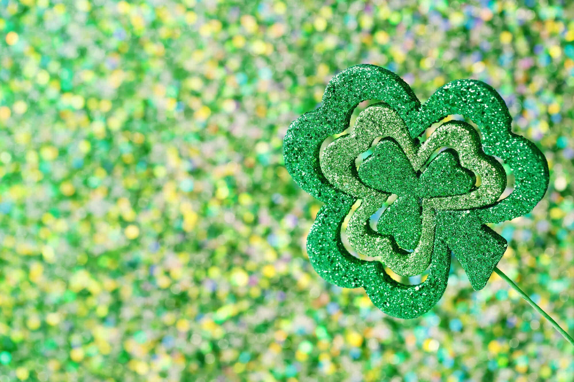 St Patrick's Day 桌布 壁紙 — 閃閃發光的綠色三葉草剪影在閃爍的綠色和黃色散景背景上脫穎而出。