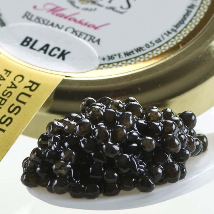 Black Caviar 桌布 壁紙 — 閃閃發光的黑色魚子醬珍珠從一個標有俄羅斯奧塞特拉的高級罐子中灑落在純白色的盤子上。