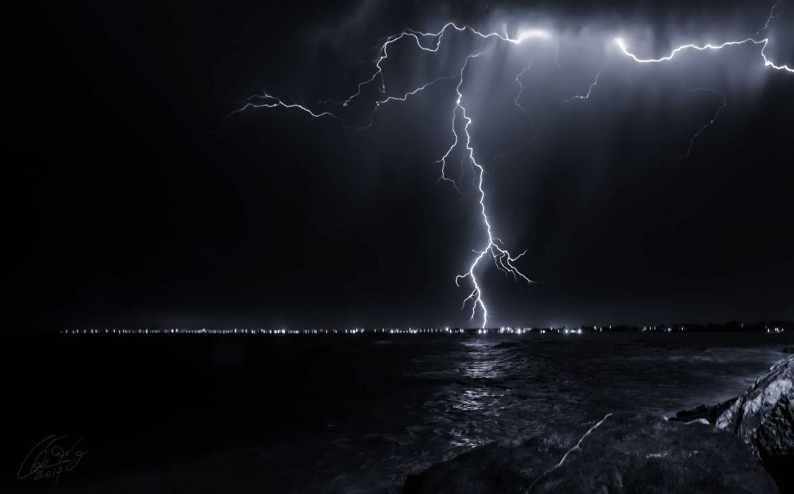 閃電照亮夜間暴風雨的海洋，遠處有城市燈光。