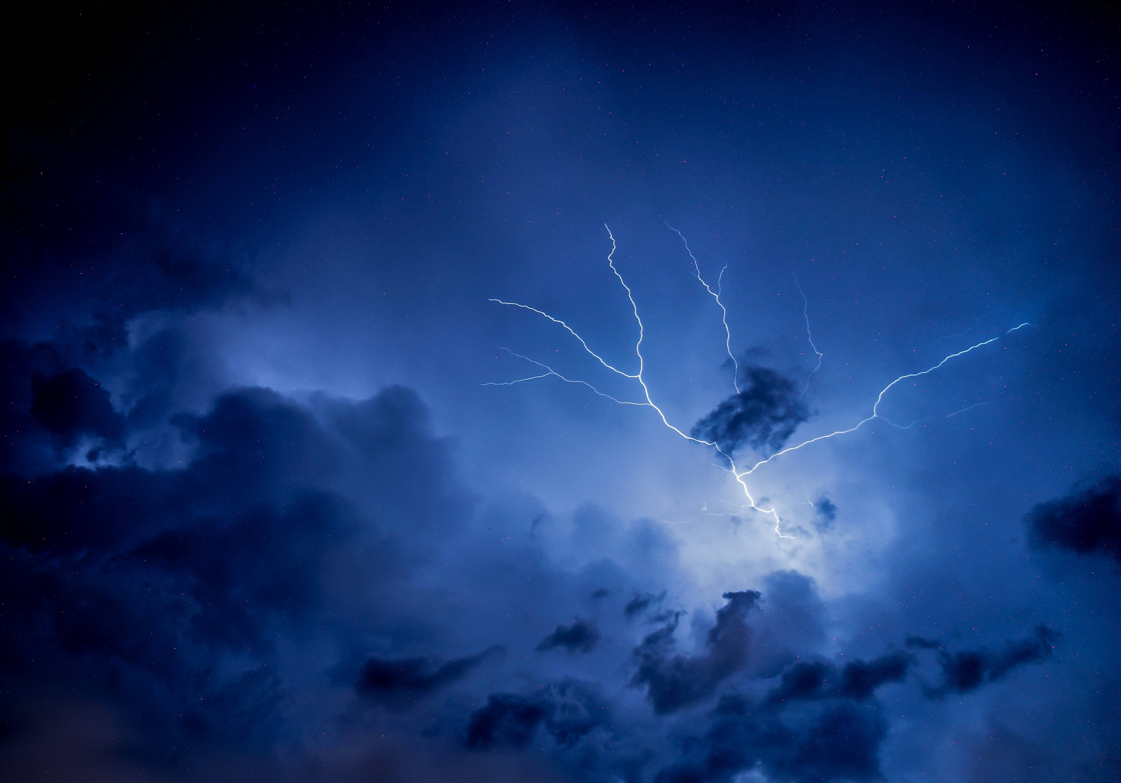 閃電雲背景 壁紙 — 一道明亮的閃電在佈滿深藍色雲層和遙遠星光的暴風雨夜空中分叉。