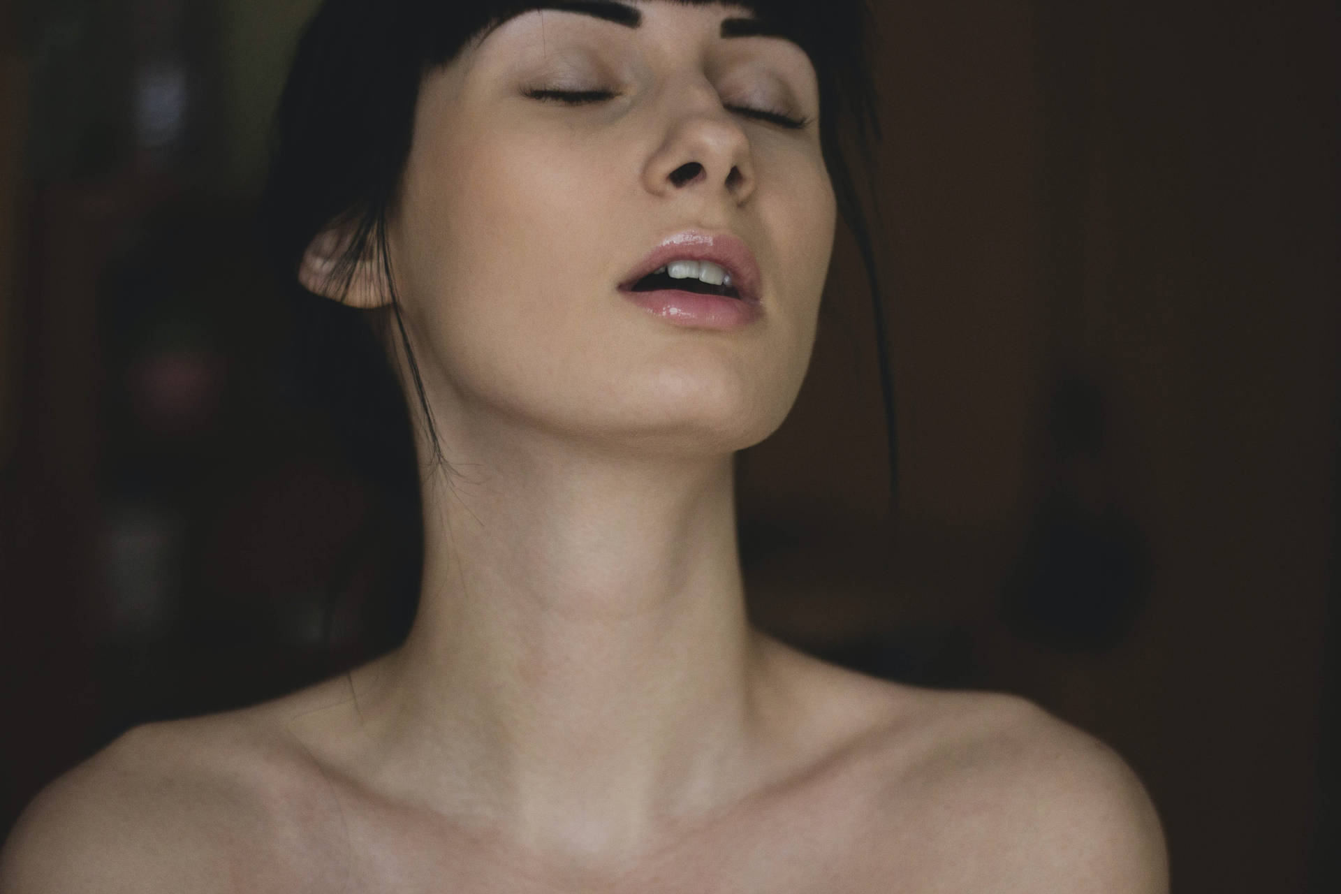 一位閉著眼睛、頭向後傾的女性在昏暗的房間裡。