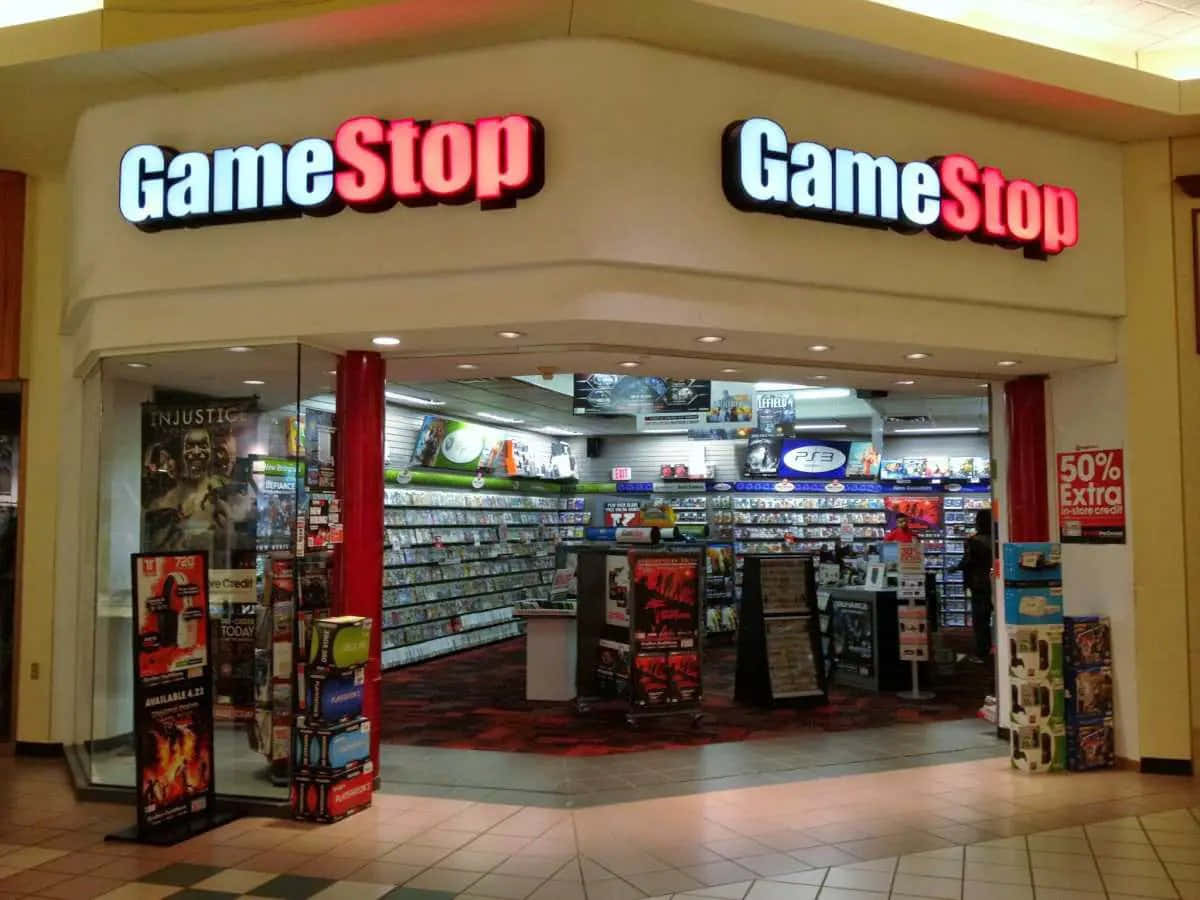 開始您的遊戲之旅！ 壁紙 — 購物中心內一間GameStop店舖入口，光線明亮，有紅色柱子和擺滿電子遊戲及主機的貨架。