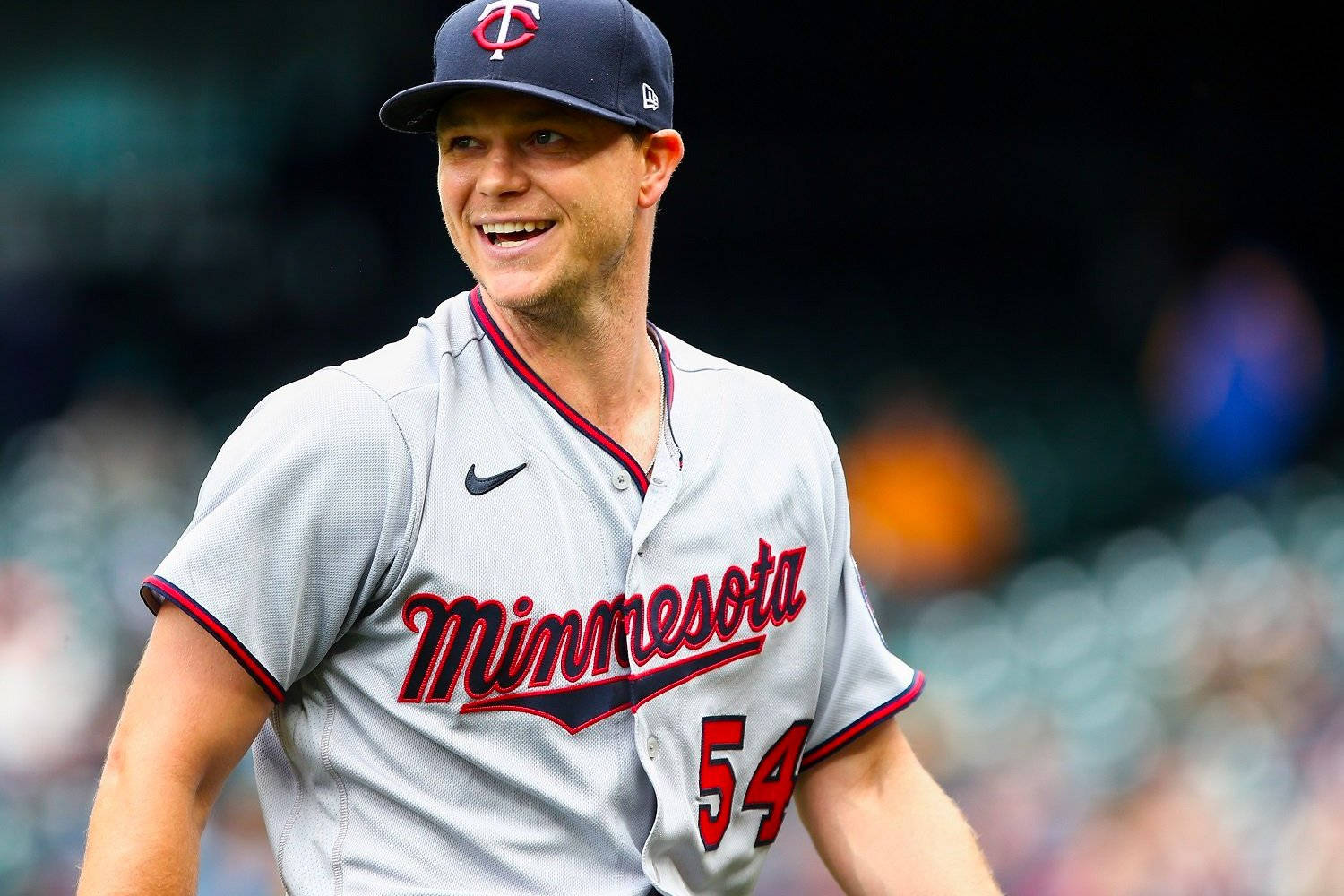 開心的 Sonny Gray 壁紙 — 一名明尼蘇達雙城棒球運動員身穿灰色鑲紅邊的球衣，戴著印有球隊標誌的海軍藍帽子，露出燦爛的笑容。