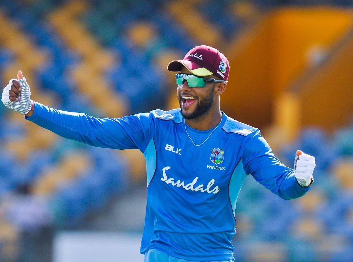 開心的沙伊·霍普 壁紙 — 一位身穿藍色Windies球衣的快樂板球運動員在體育場燈光下張開雙臂，露出燦爛笑容慶祝。