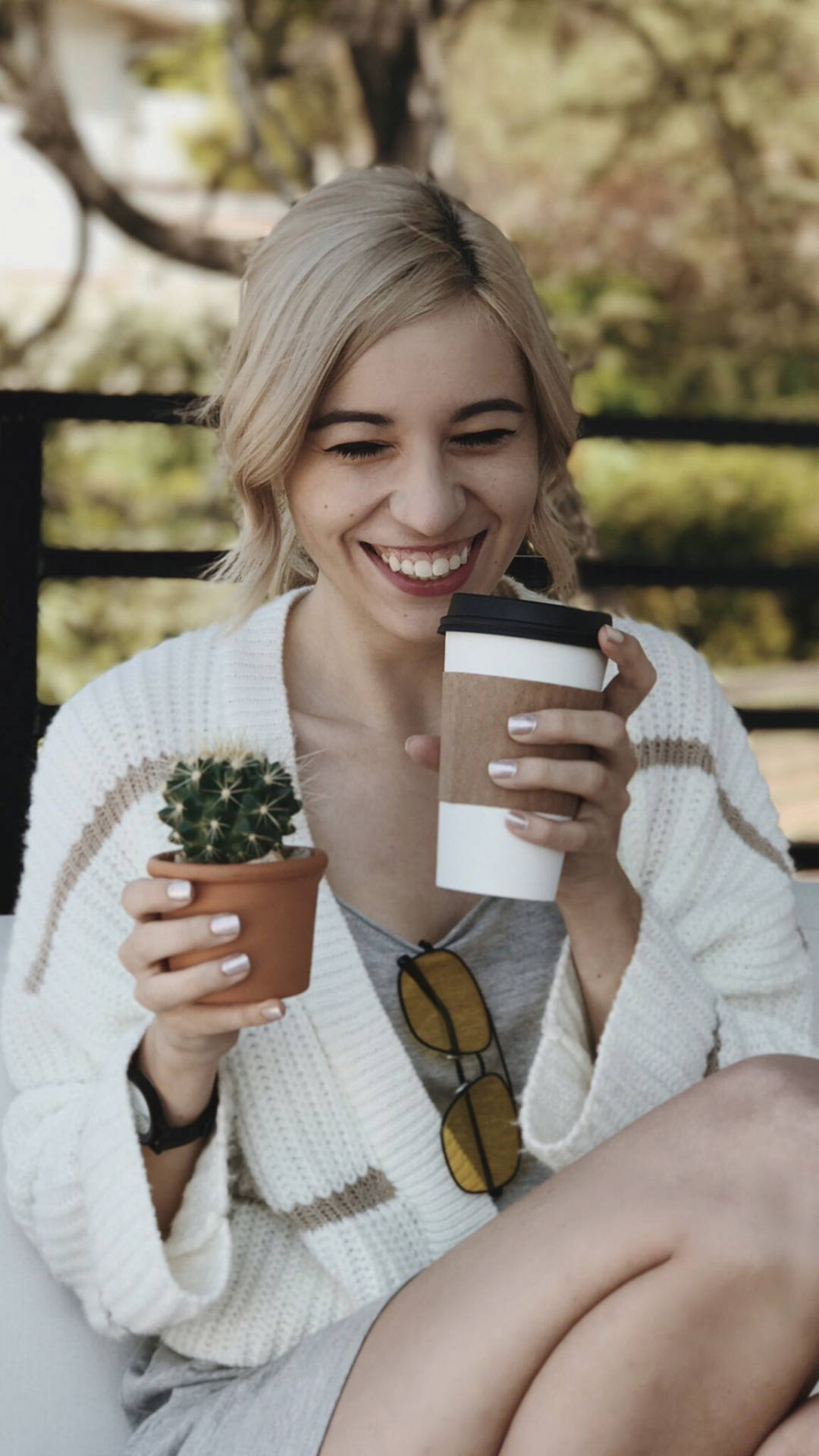 一位快樂的女性在戶外手持咖啡和仙人掌植物。