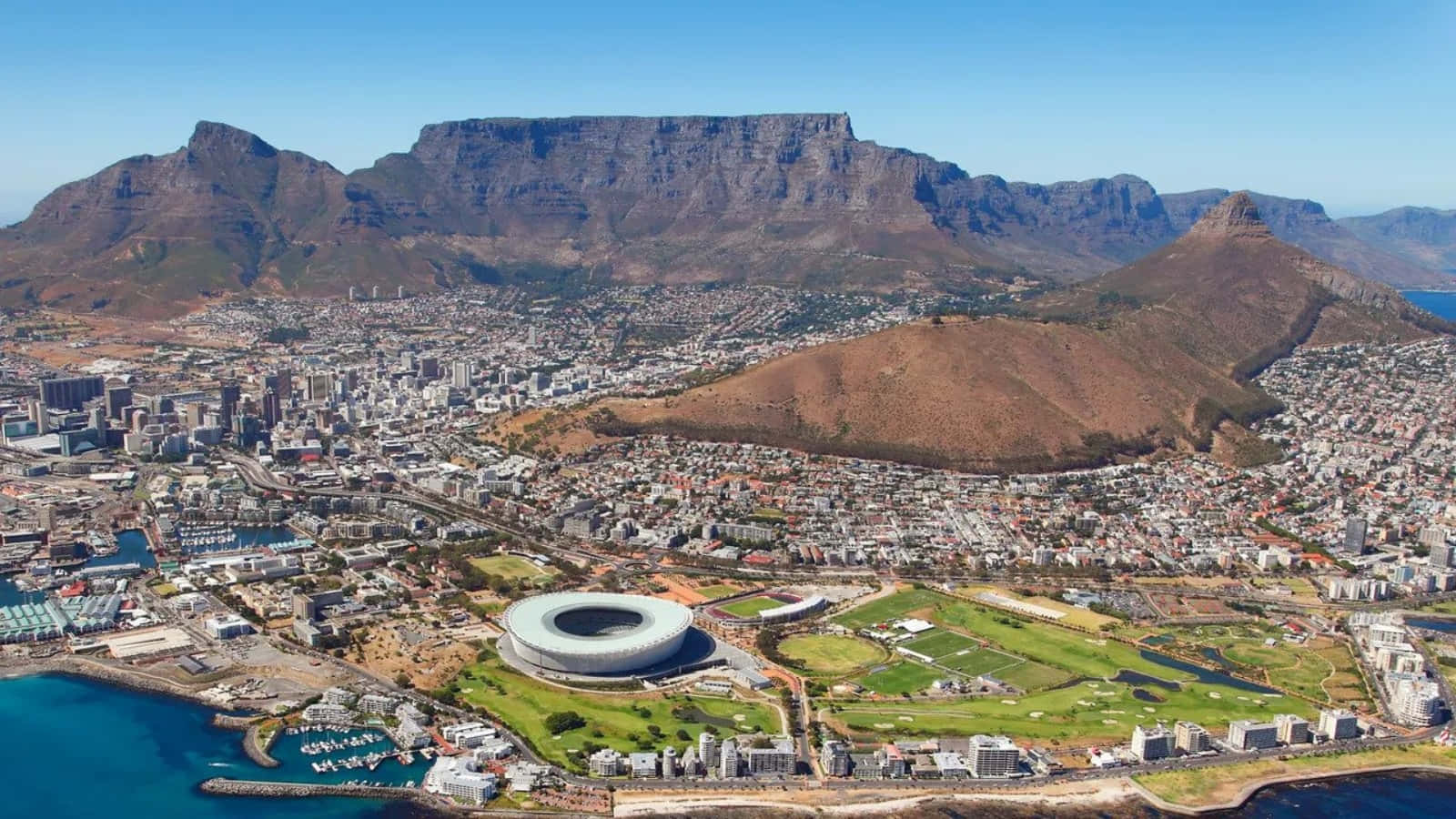 South Africa 桌布 壁紙 — 開普敦的鳥瞰圖，桌山聳立在廣闊的城市景觀和海岸線附近的現代體育場之上。