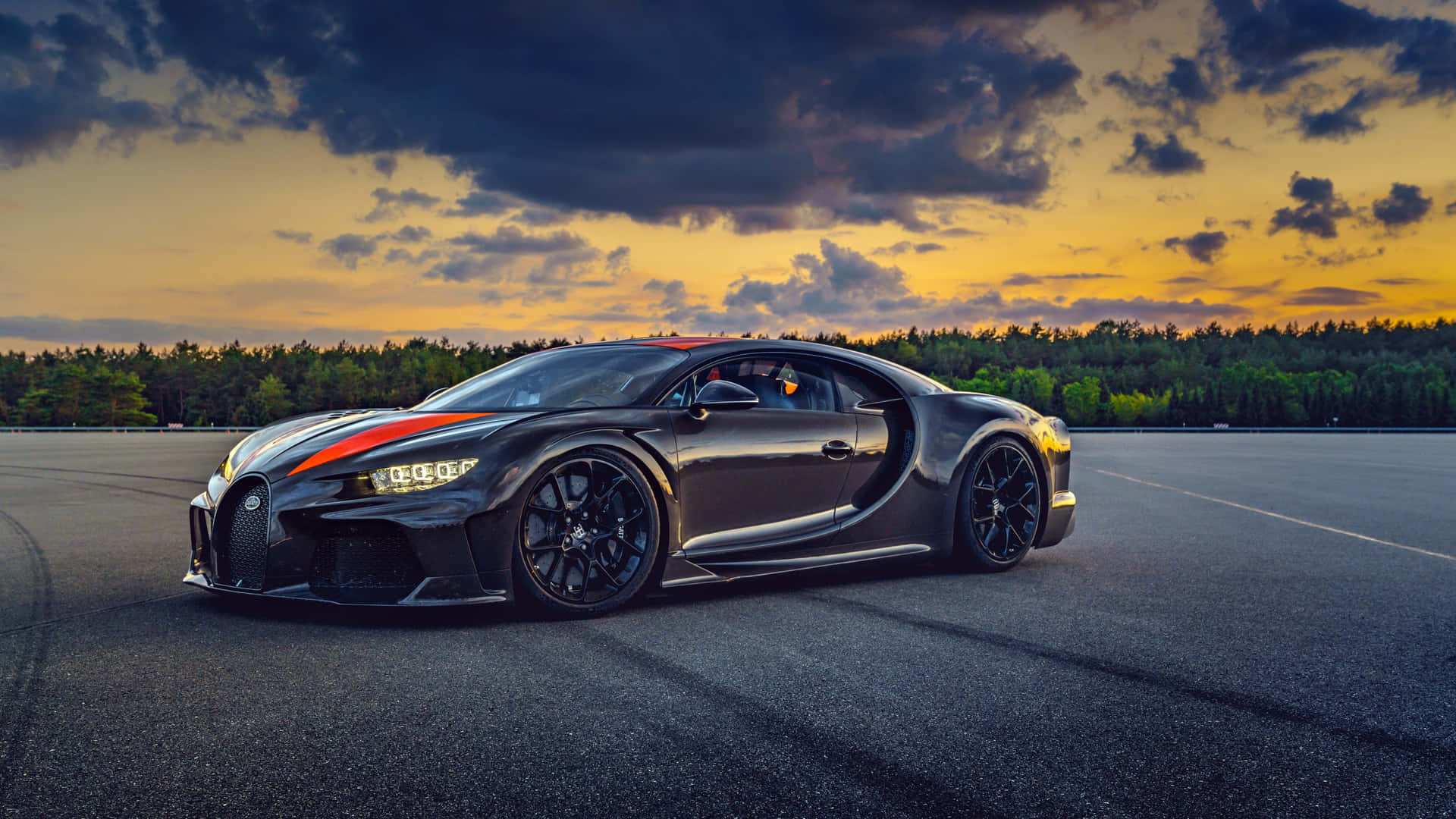 日落時分賽道上帶有橙色條紋的黑色Bugatti Chiron。