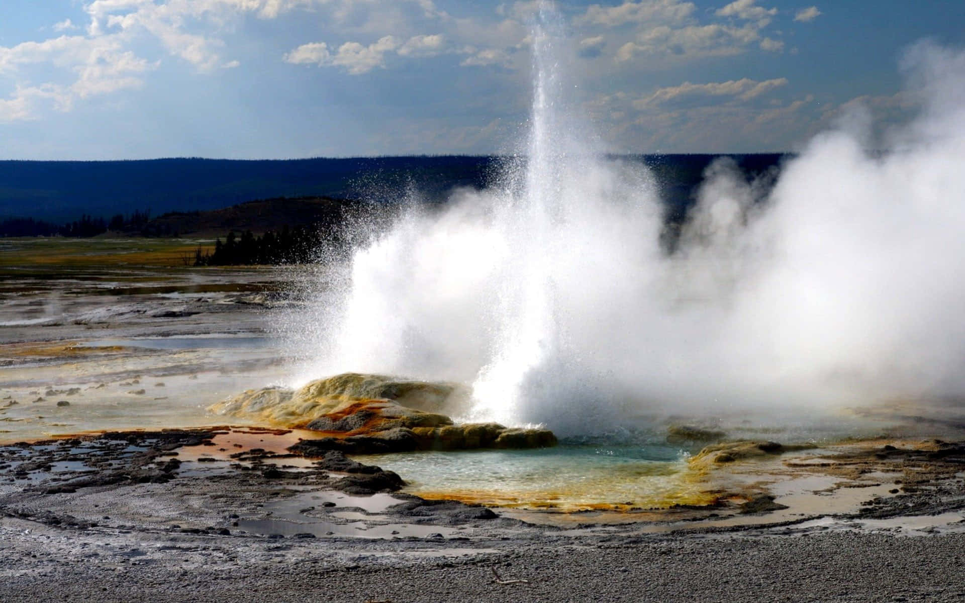 Yellowstone Geysers 桌布 壁紙 — 間歇泉噴出強勁的蒸氣和水柱，背景是藍天和遠山。