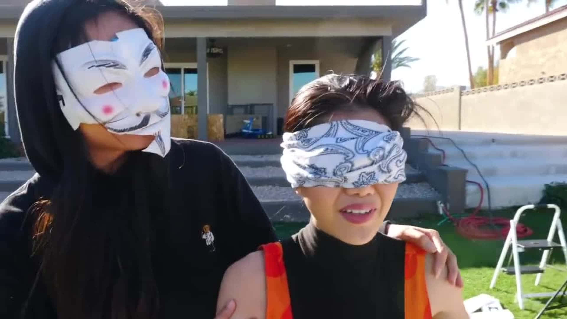 兩個人在戶外，一人戴著白色蓋伊·福克斯面具，另一人用圖案頭巾矇住眼睛。