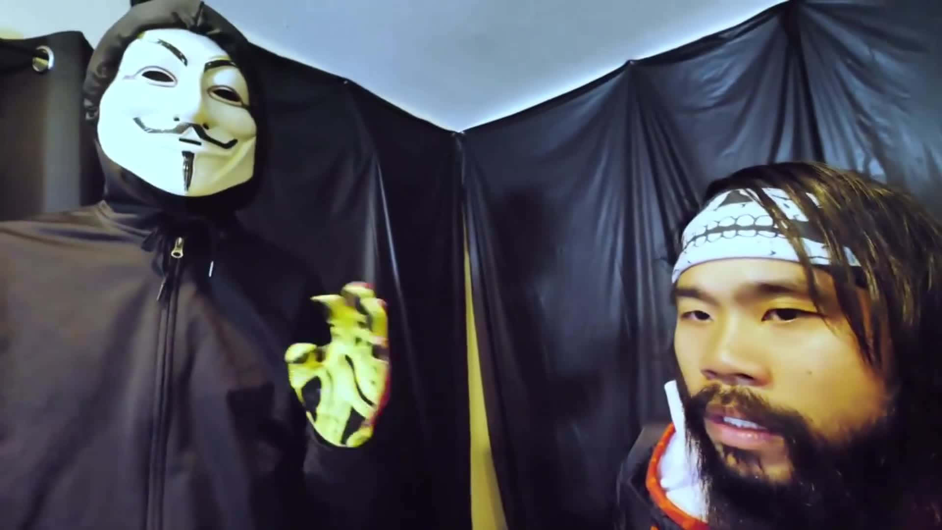 戴蓋伊·福克斯面具的人拿著發光的心臟，旁邊是留鬍子、戴頭帶的男人。